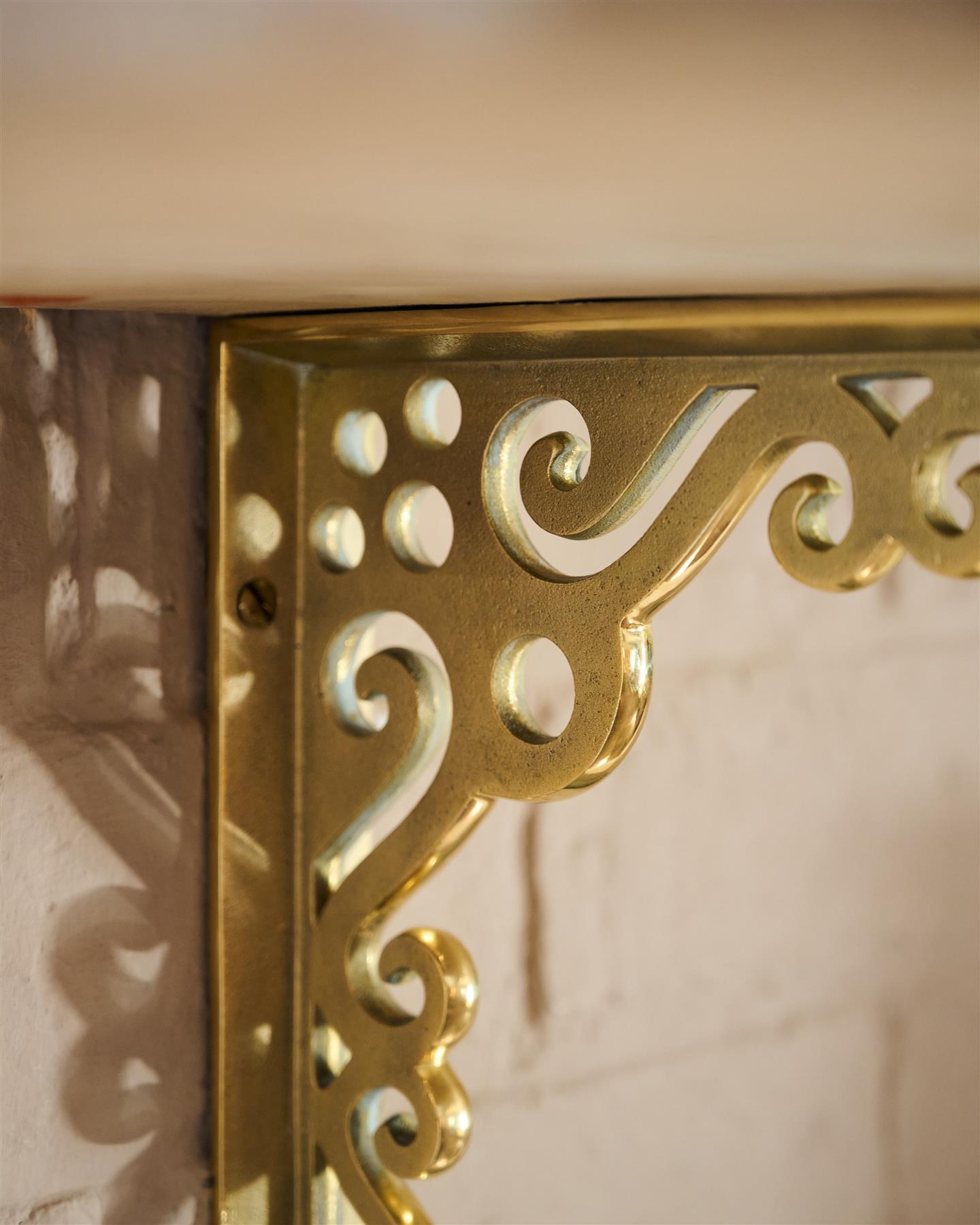 A close-up oblique view of the decorative cutout patterns on a large Victorian-inspired ornate aged brass shelf bracket.