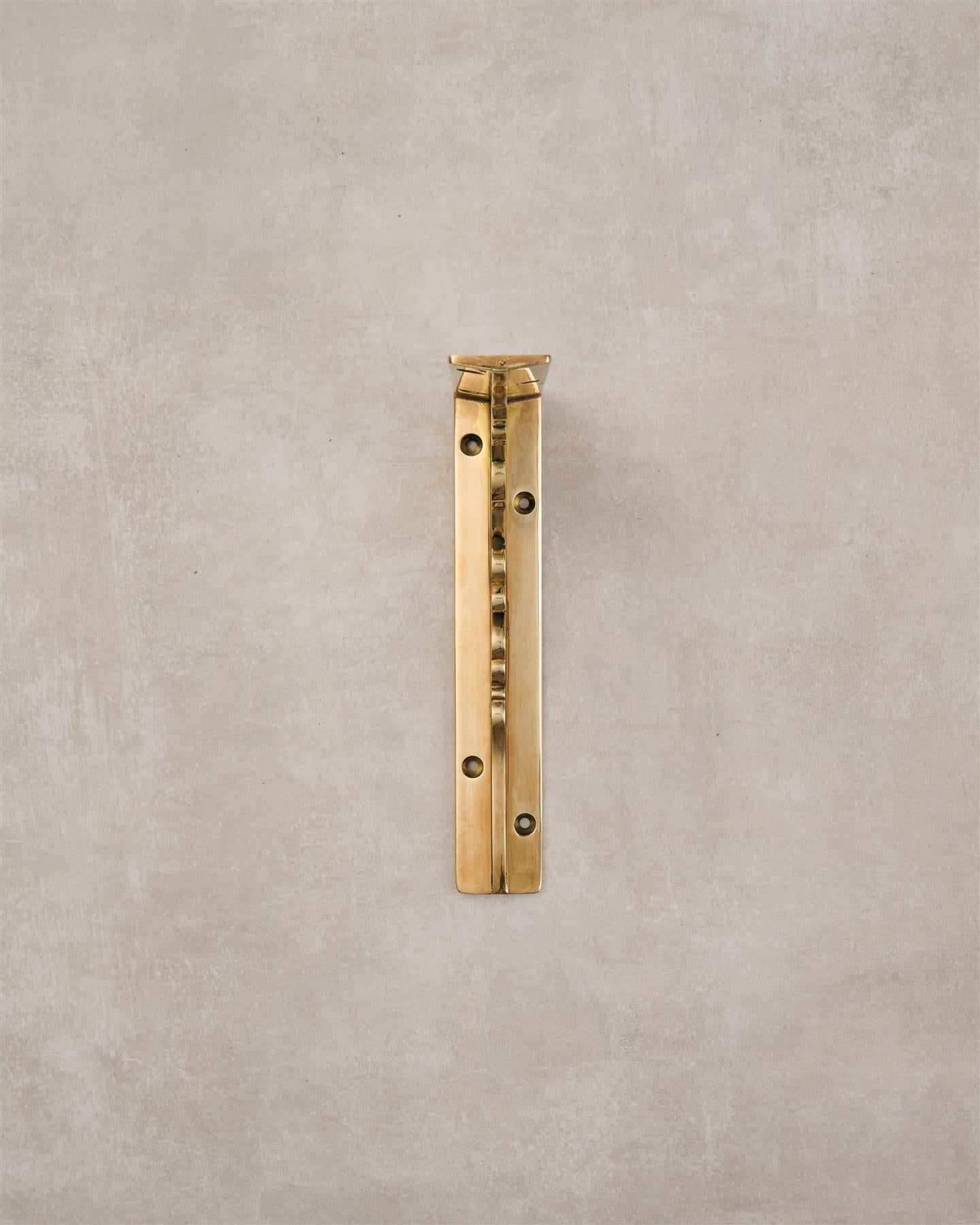 A front profile view of a small Victorian-inspired ornate shelf bracket in a warm polished brass finish.