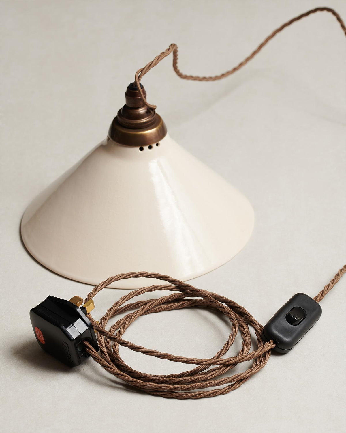 A small plug-in light with a cream glazed shade, brown twisted fabric flex cord, brass fittings and a black plastic switch and plug. TEST