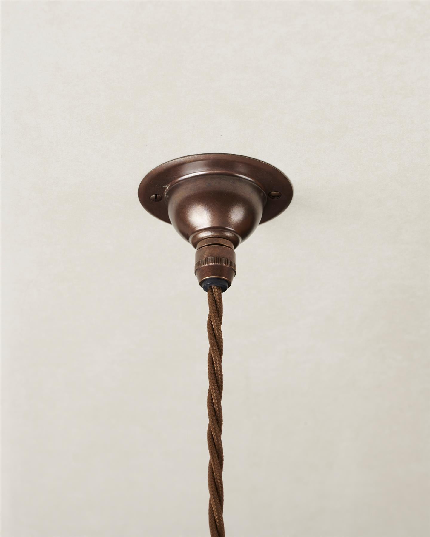 A small aged brass ceiling rose with a brown twisted fabric flex cord.