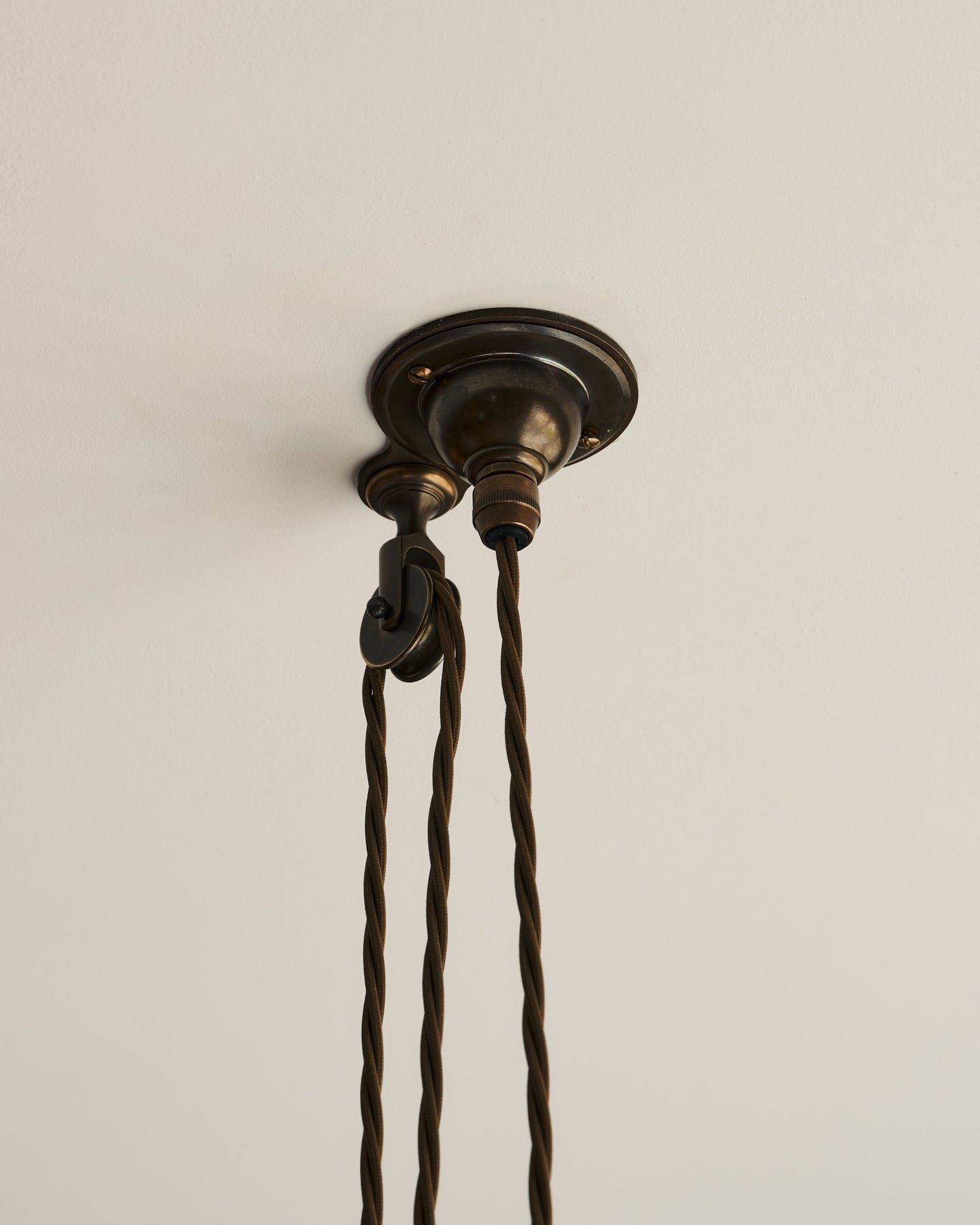 A small aged brass ceiling rose with a wheel pulley and a brown twisted fabric flex cord.