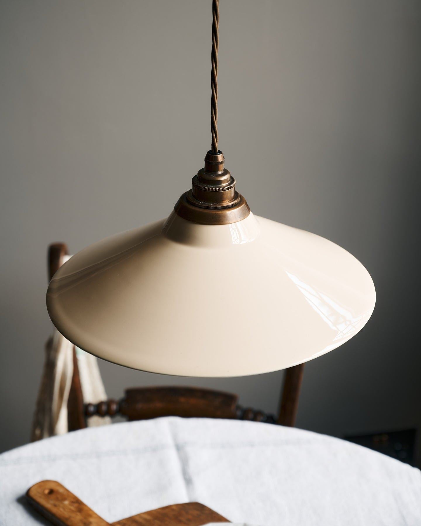 A close-up view of a small cream glazed ceramic shade with aged brass fittings and brown twisted fabric flex cord.