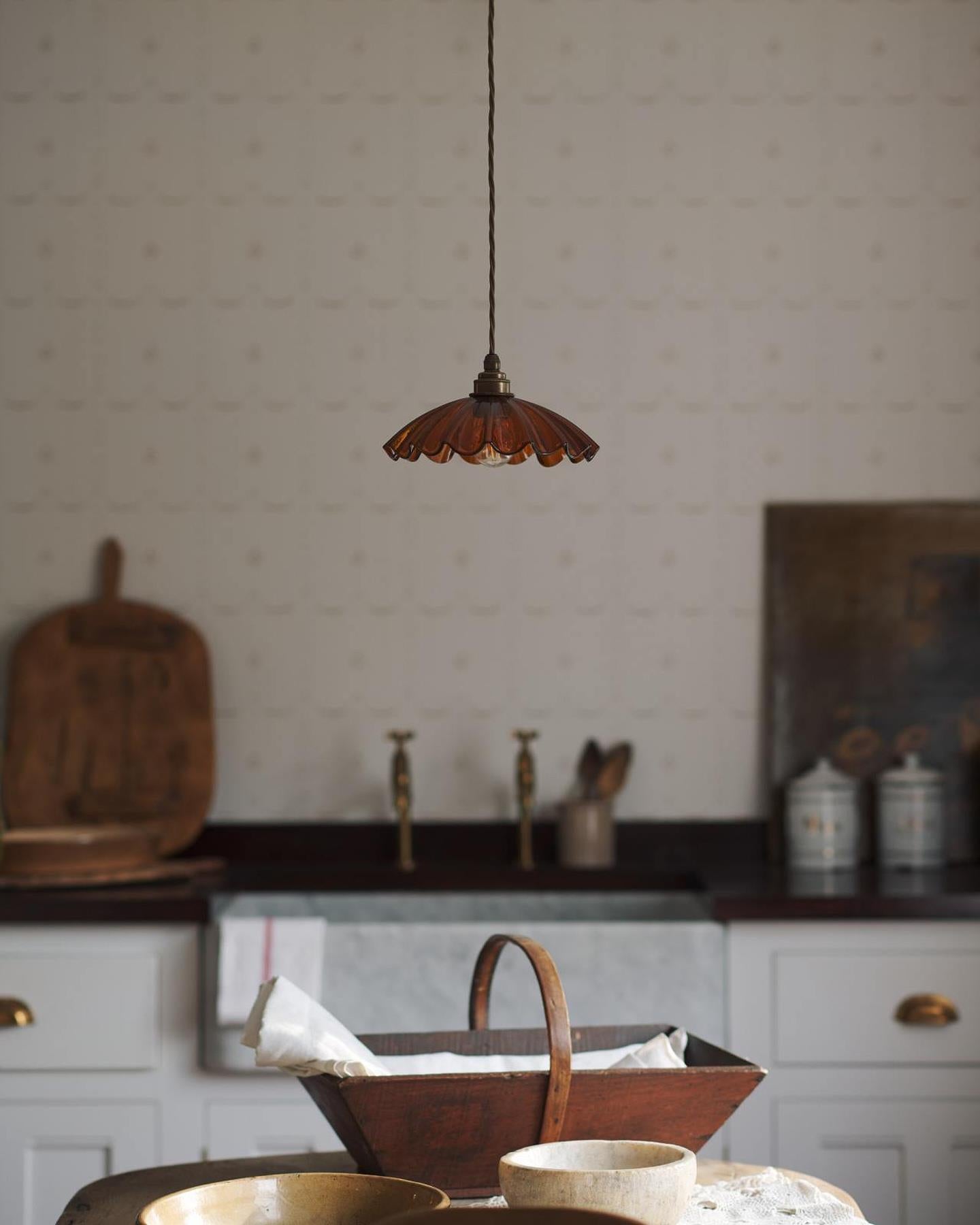 A small frilly amber glass pendant light with brass fittings and brown twisted fabric flex cord. The light is off.