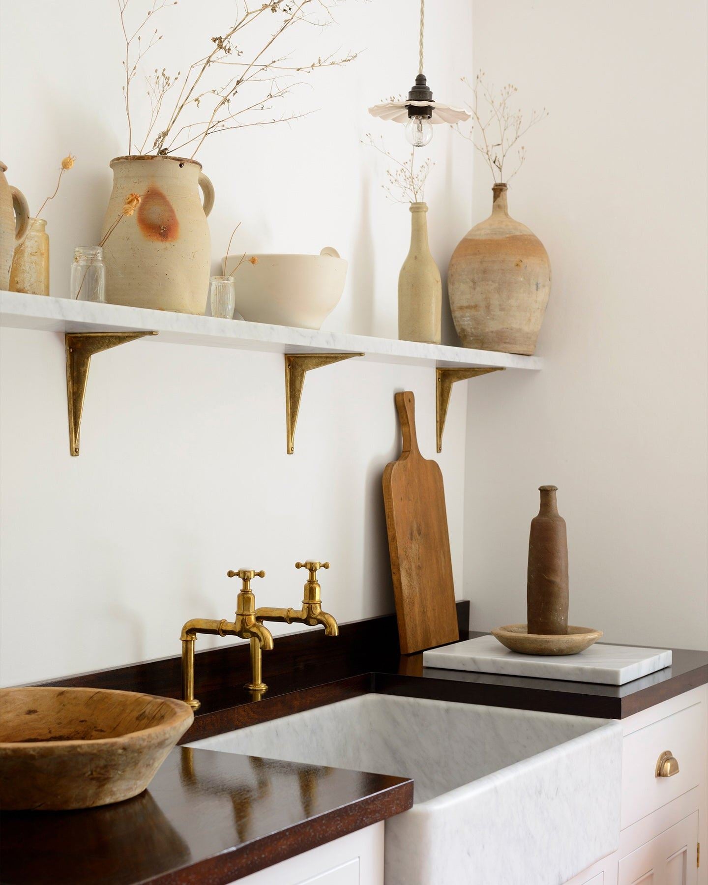 An oblique view of a small pleated porcelain light hanging over a Carrara marble sink.