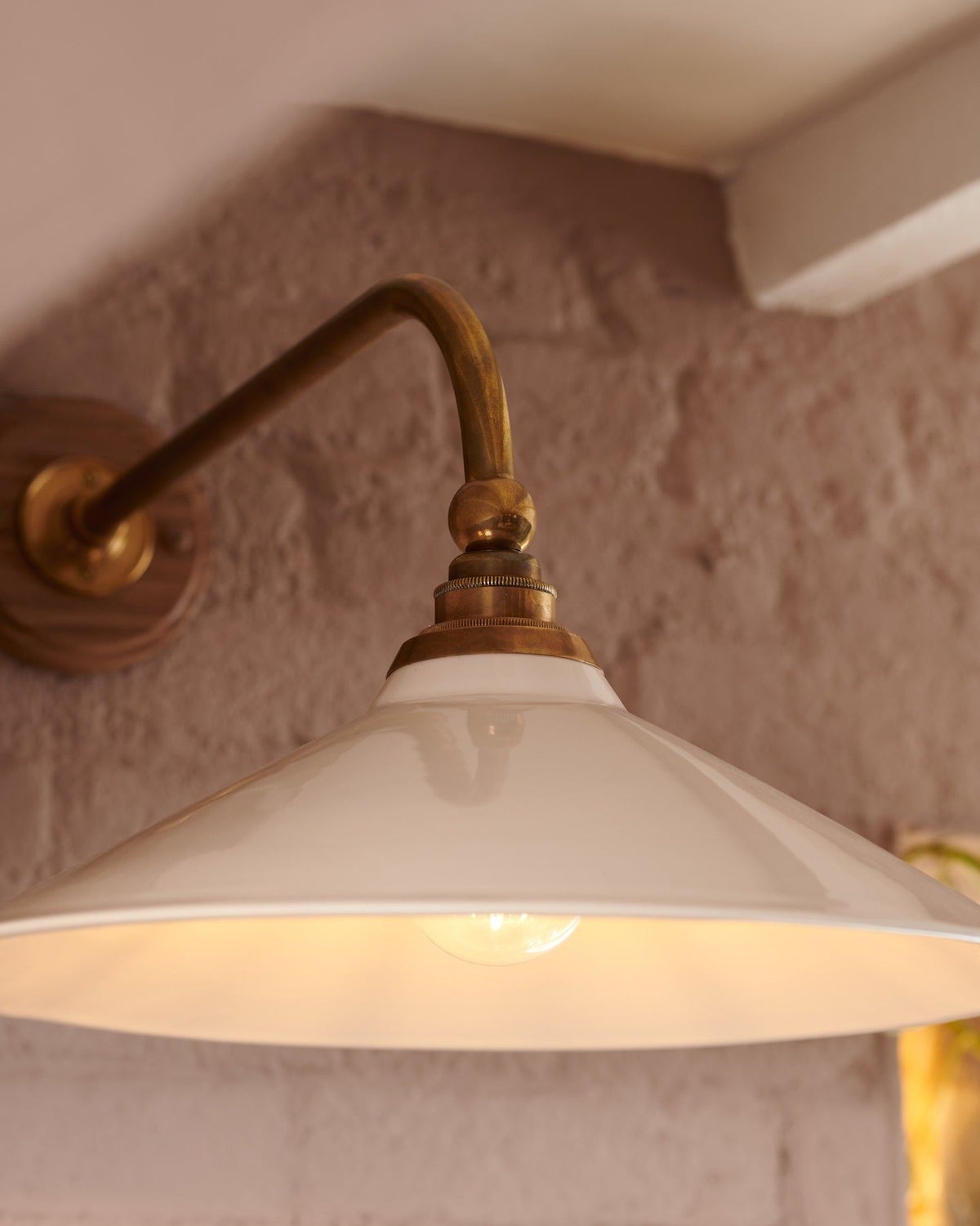 A close-up view of a large Victorian-inspired wall light with a brass arm and a cream glazed ceramic shade. TEST
