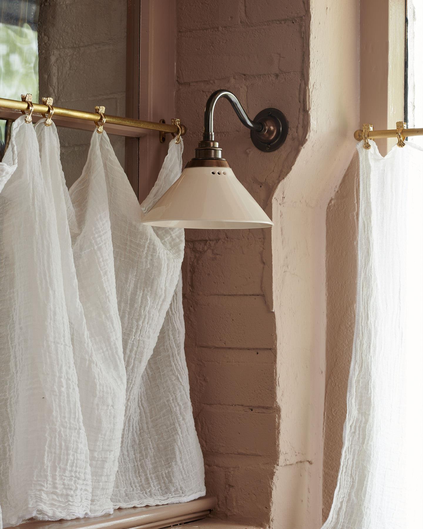 An atmospheric cottage room with pink brick walls, beamed ceiling and small wall lights either side of a window.