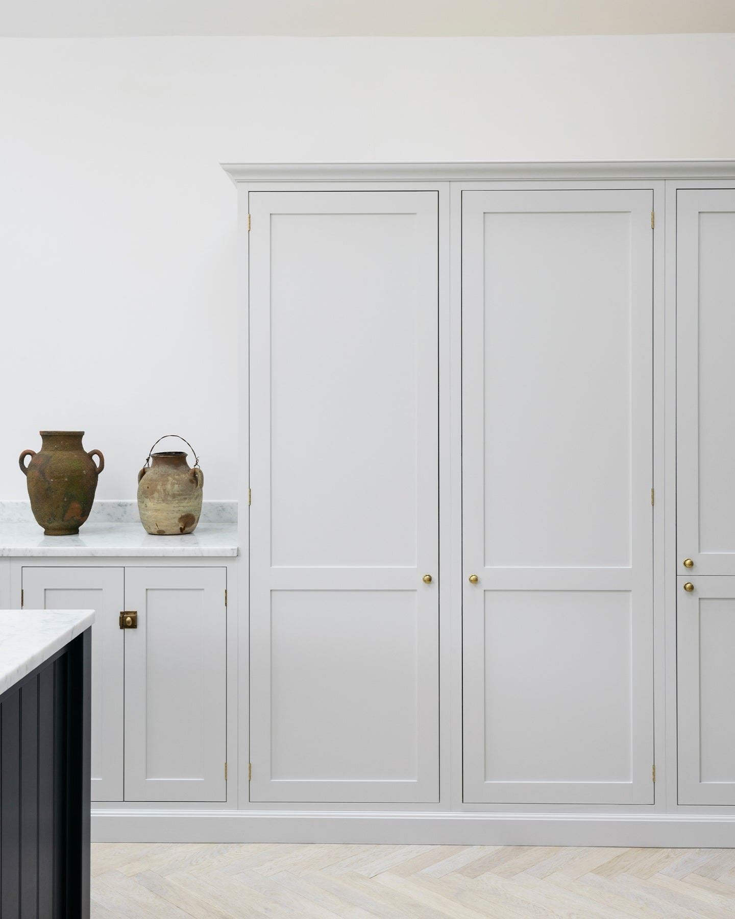A straight-on view of a simple Shaker-style kitchen with off-white painted tall pantry cupboards and white walls.