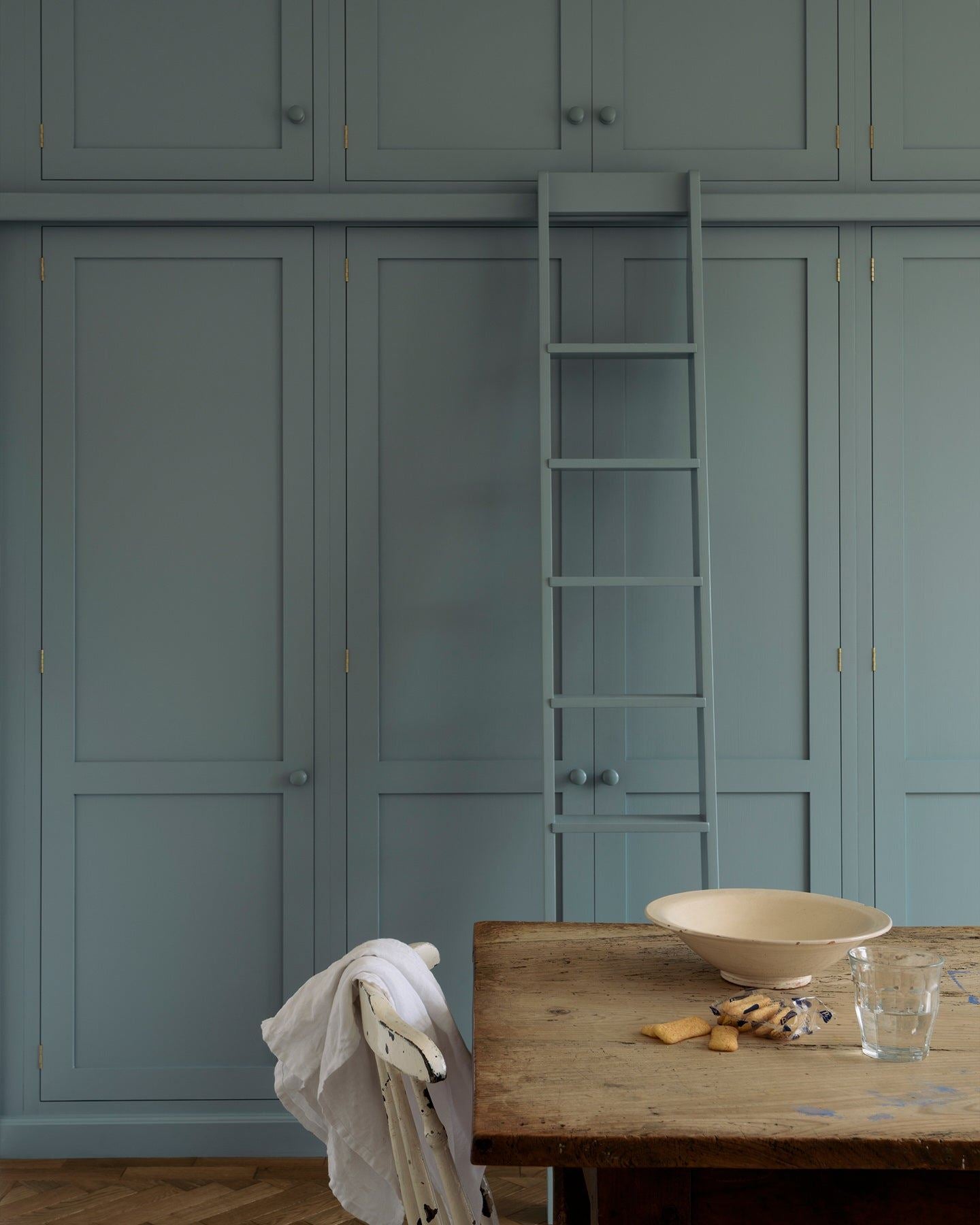 A straight-on view of a tall bank of duck-egg blue painted Shaker-style pantry cupboards with a sliding ladder.