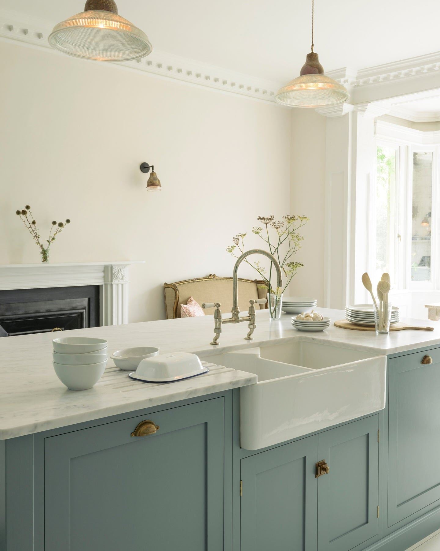 An oblique view of a duck-egg blue painted Shaker-style kitchen sink cabinet with a ceramic Belfast sink, Carrara marble worktop and white walls.