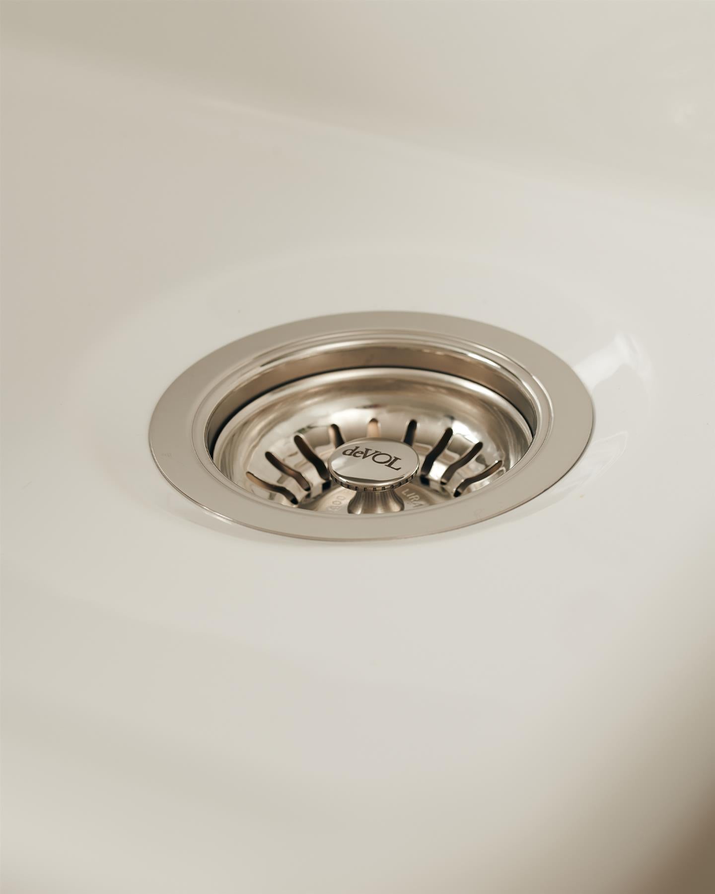A basket waste strainer in a polished chrome finish fitted in a ceramic sink.