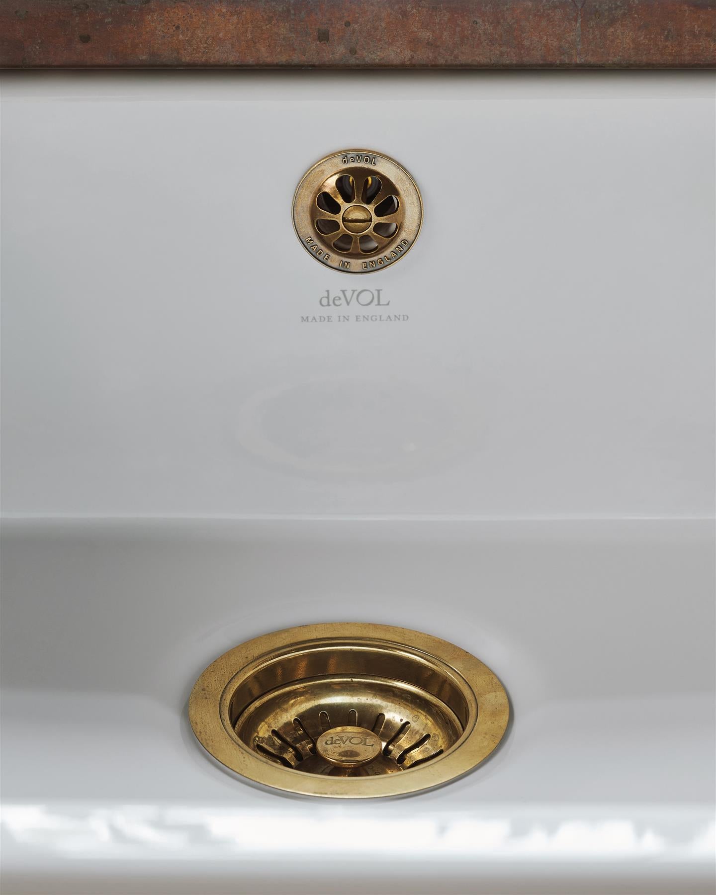 A straight-on view of a basket waste strainer with a deVOL domed overflow cap in a warm burnished brass finish, there is a small 'deVOL' logo in the middle of the waste strainer finial.