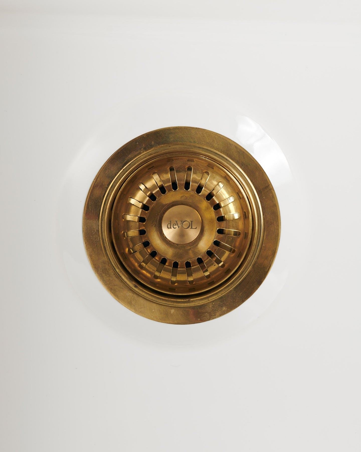 An overhead view of a basket waste strainer in a warm burnished brass finish, there is a small 'deVOL' logo in the middle of the central finial.