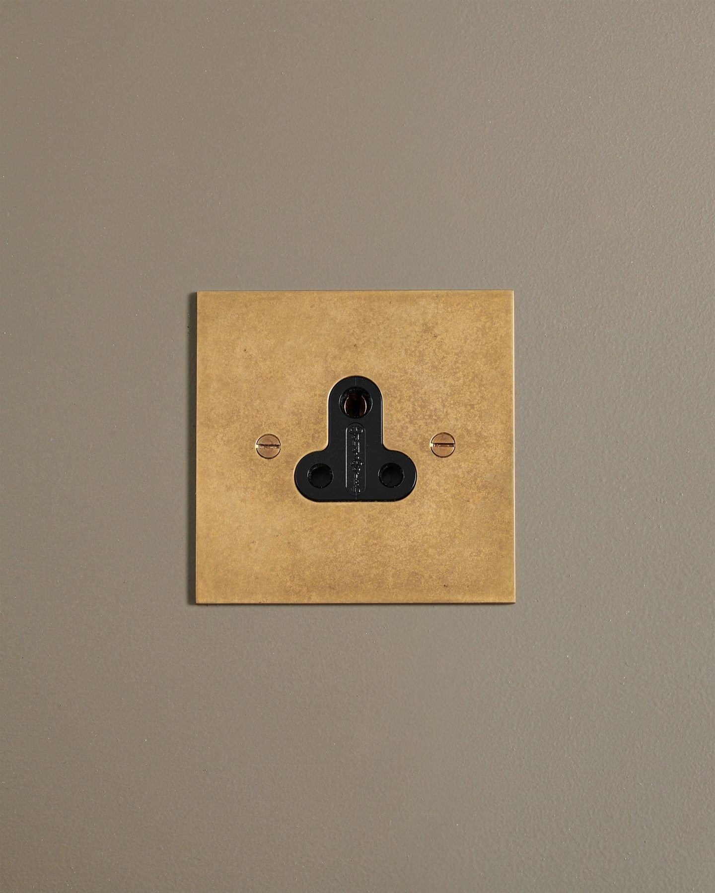 A straight-on view of a classic 5 amp single plug socket in a mottled aged brass finish.