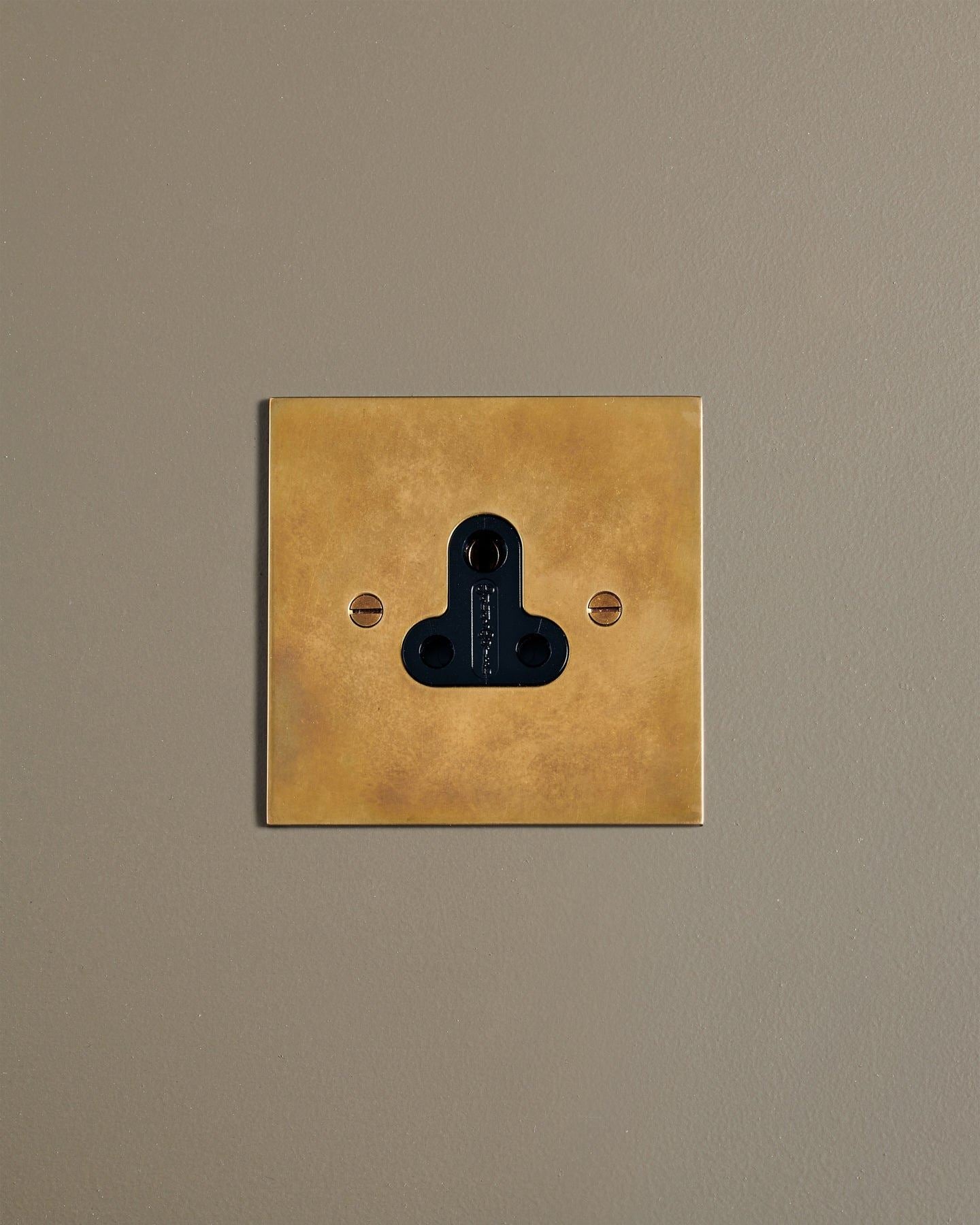 A straight-on view of a classic 5 amp single plug socket in a warm burnished brass finish.
