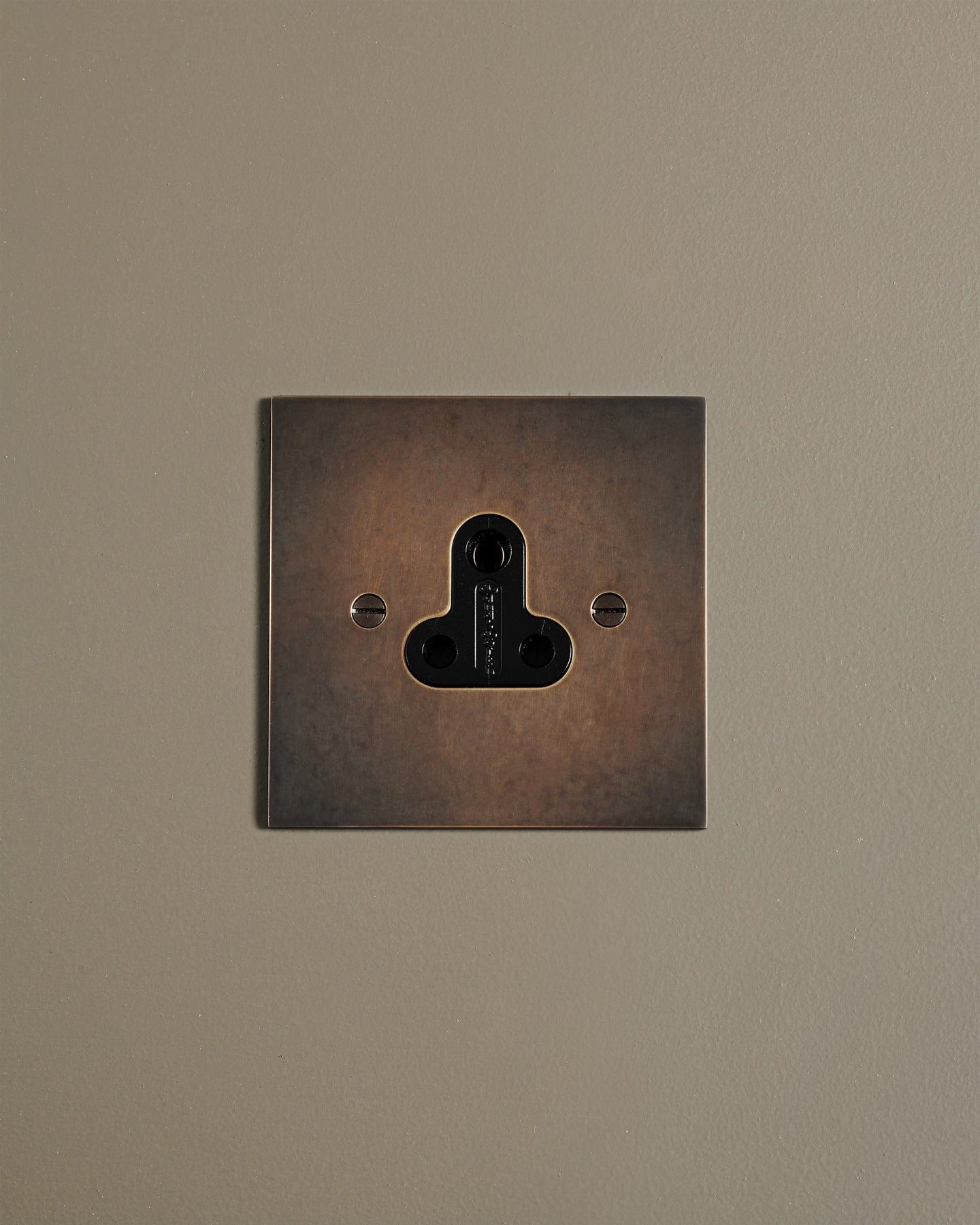 A straight-on view of a classic 5 amp single plug socket in a dark oxidised brass finish.