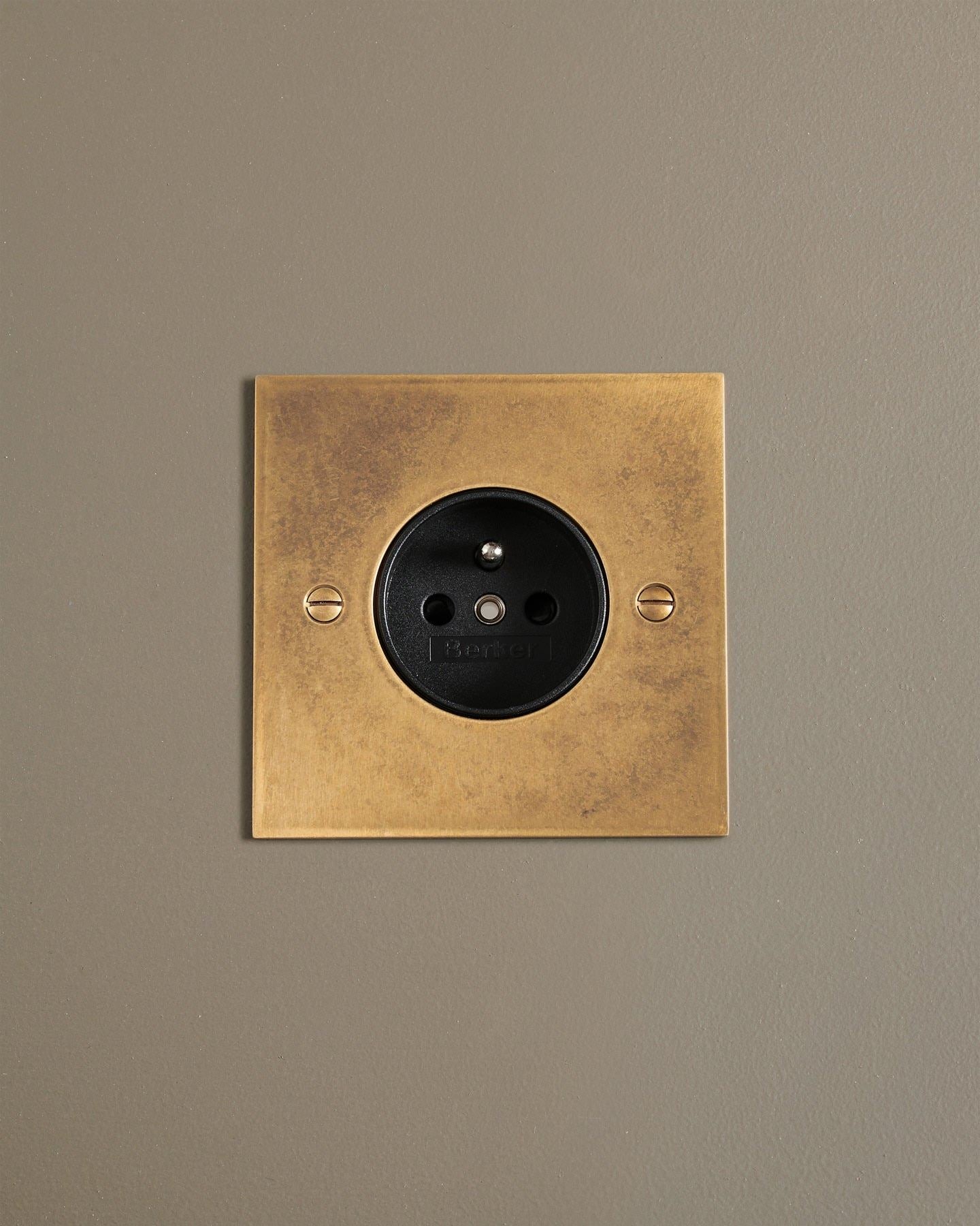 A straight-on view of a classic French-style single plug socket in a mottled aged brass finish.