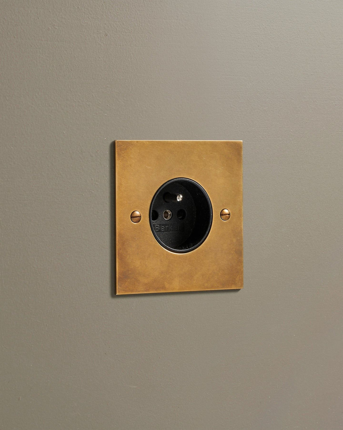 A straight-on view of a classic French-style single plug socket in a warm burnished brass finish. TEST