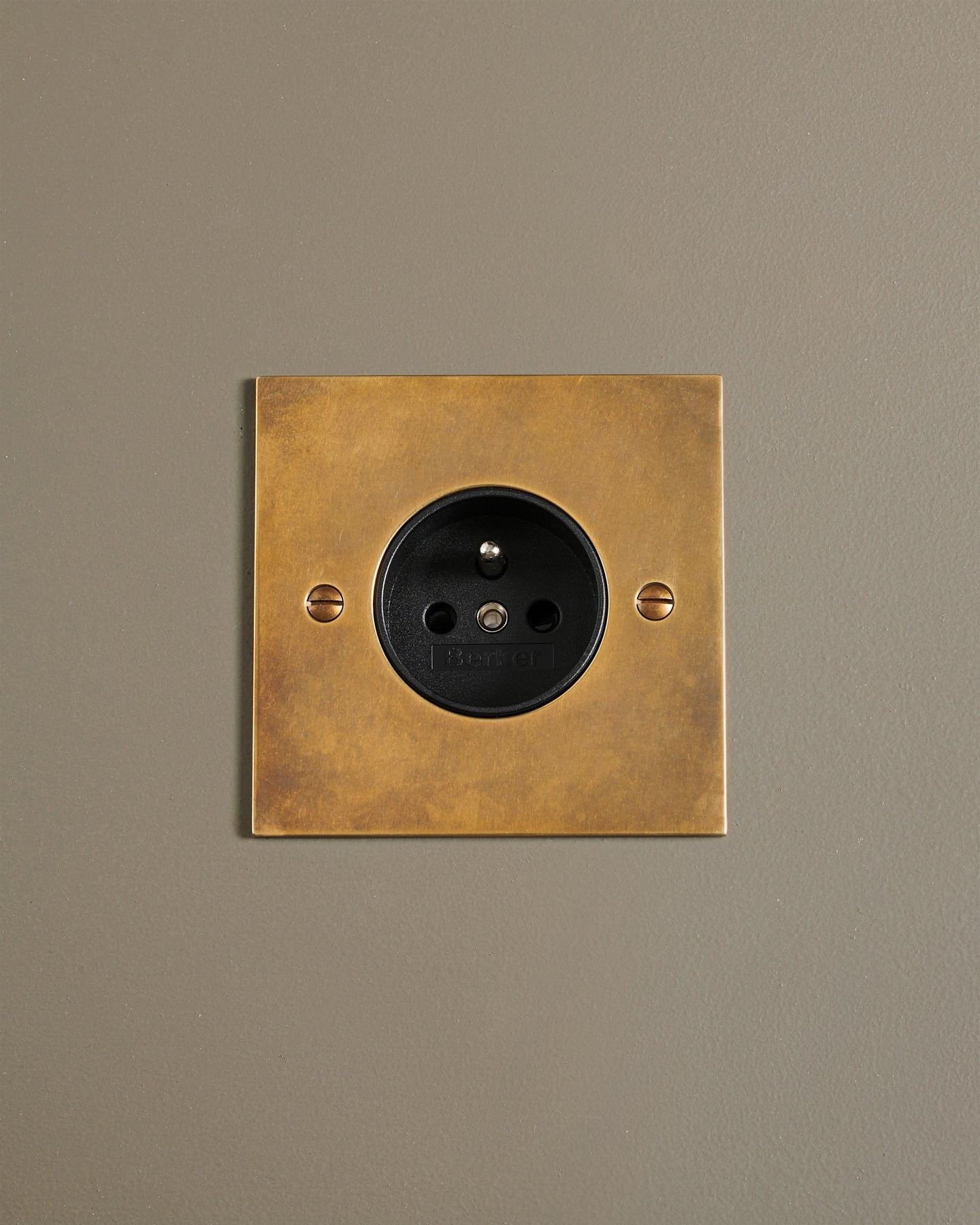 An oblique view of a classic French-style single plug socket in a warm burnished brass finish.