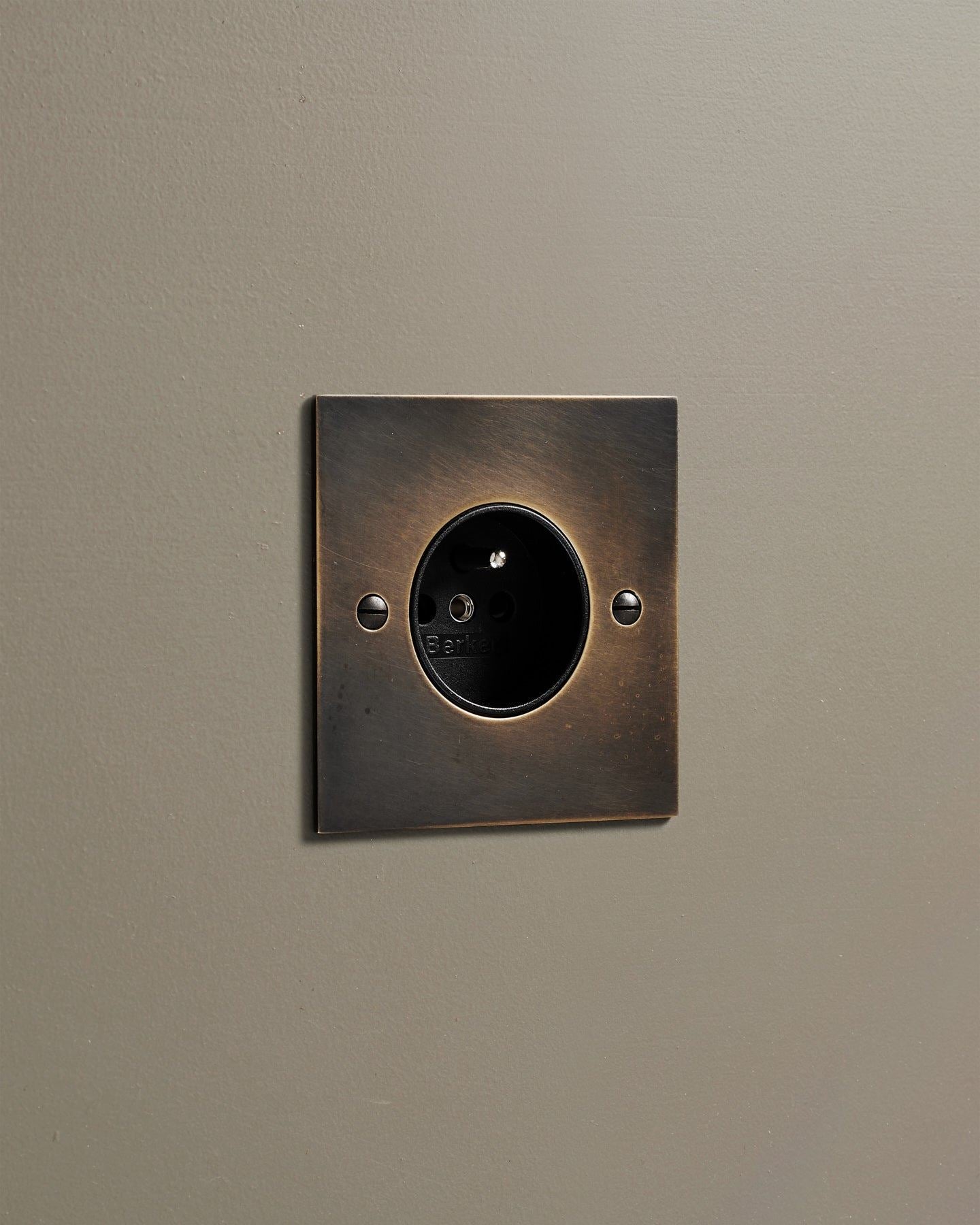 An oblique view of a classic French-style single plug socket in a dark oxidised brass finish.