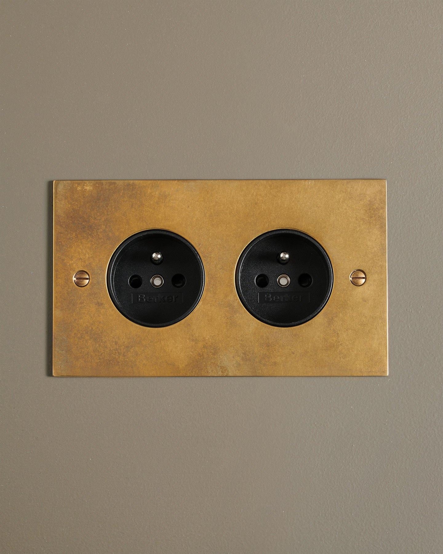 A straight-on view of a classic French-style twin plug socket in a warm burnished brass finish.