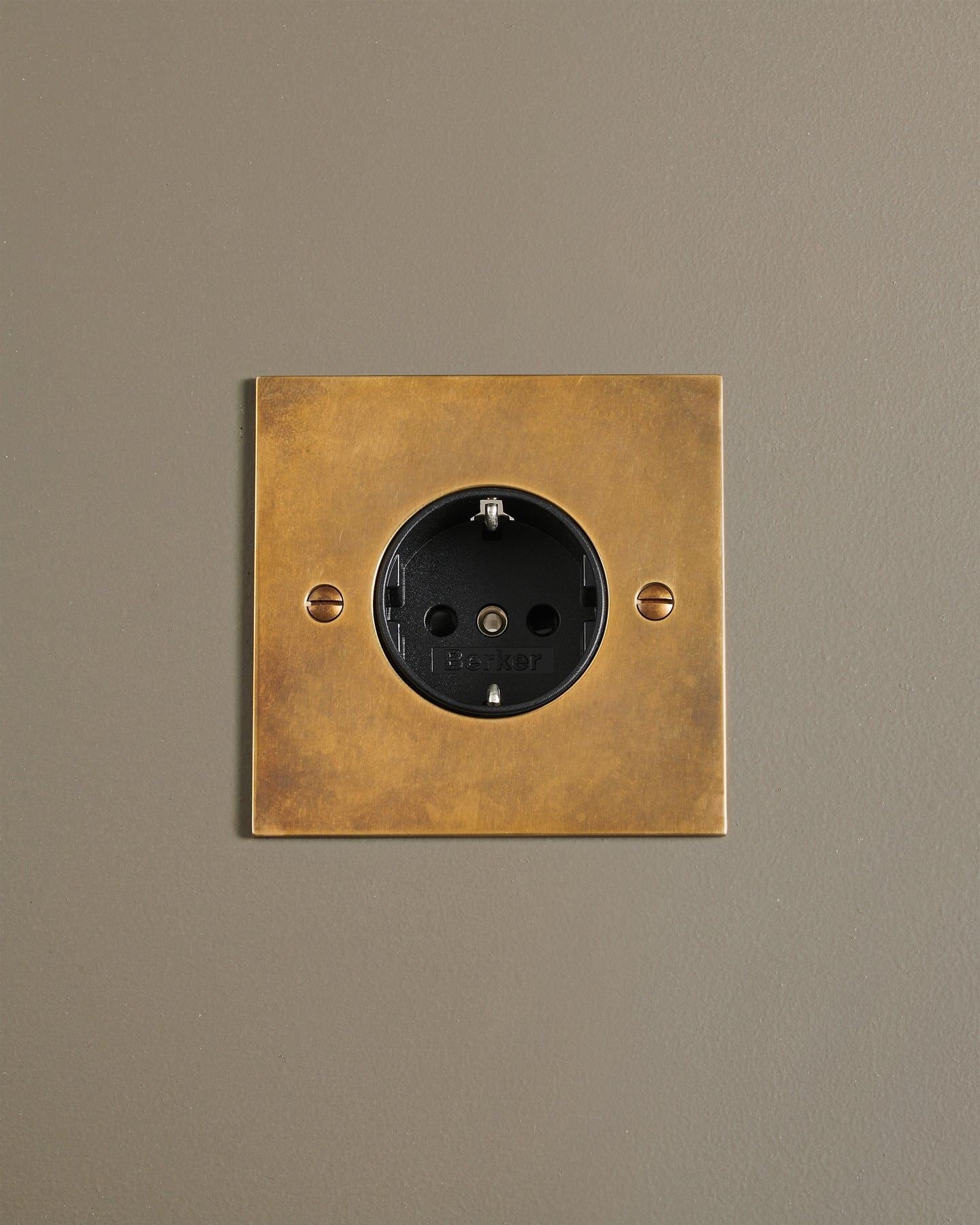 A straight-on view of a classic Schuko-style single plug socket in a warm burnished brass finish.