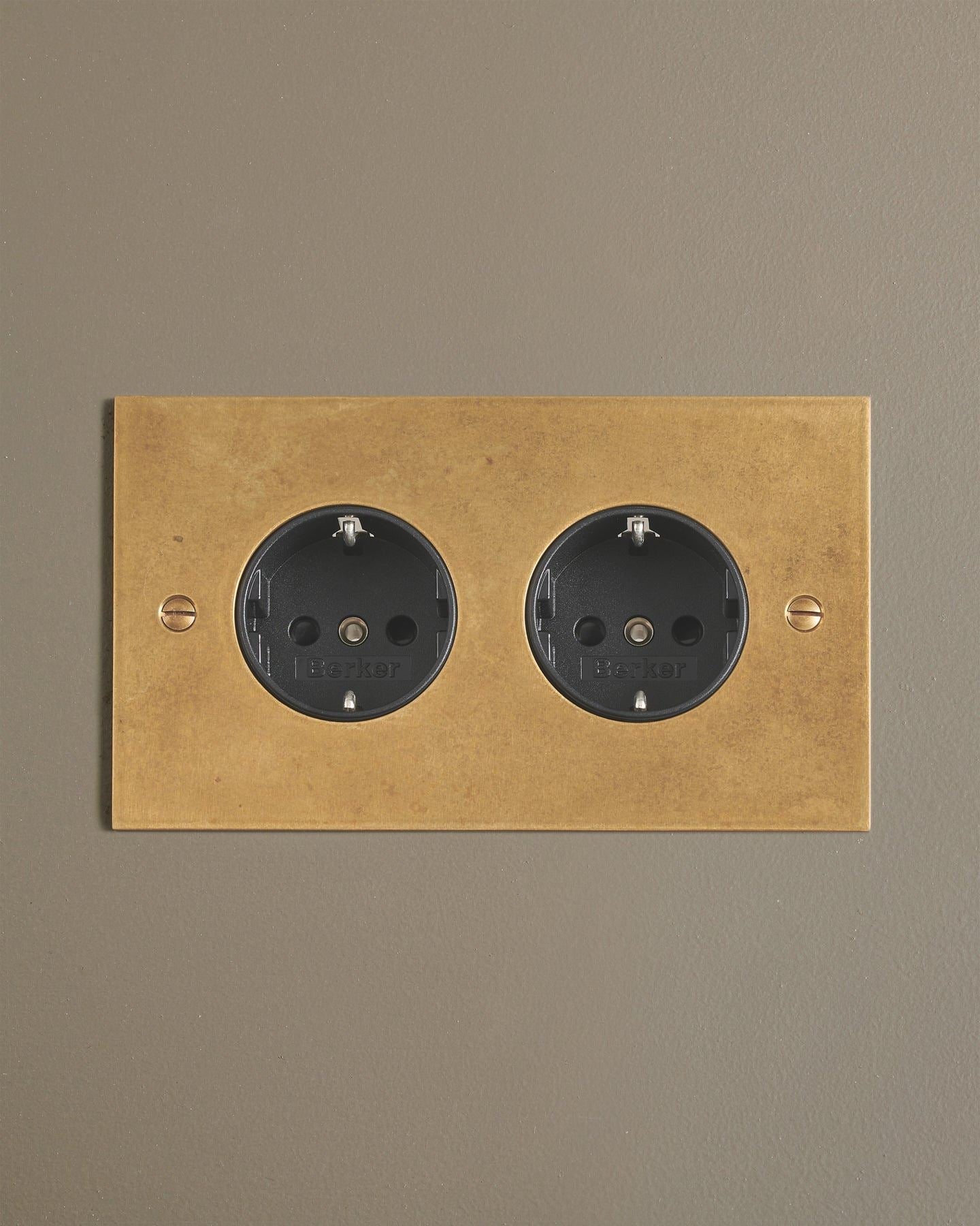 A straight-on view of a classic Schuko-style twin plug socket in a mottled aged brass finish.