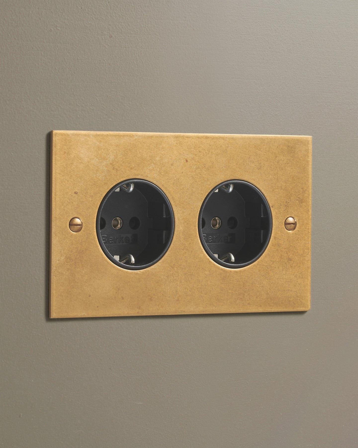 An oblique view of a classic Schuko-style twin plug socket in a mottled aged brass finish.