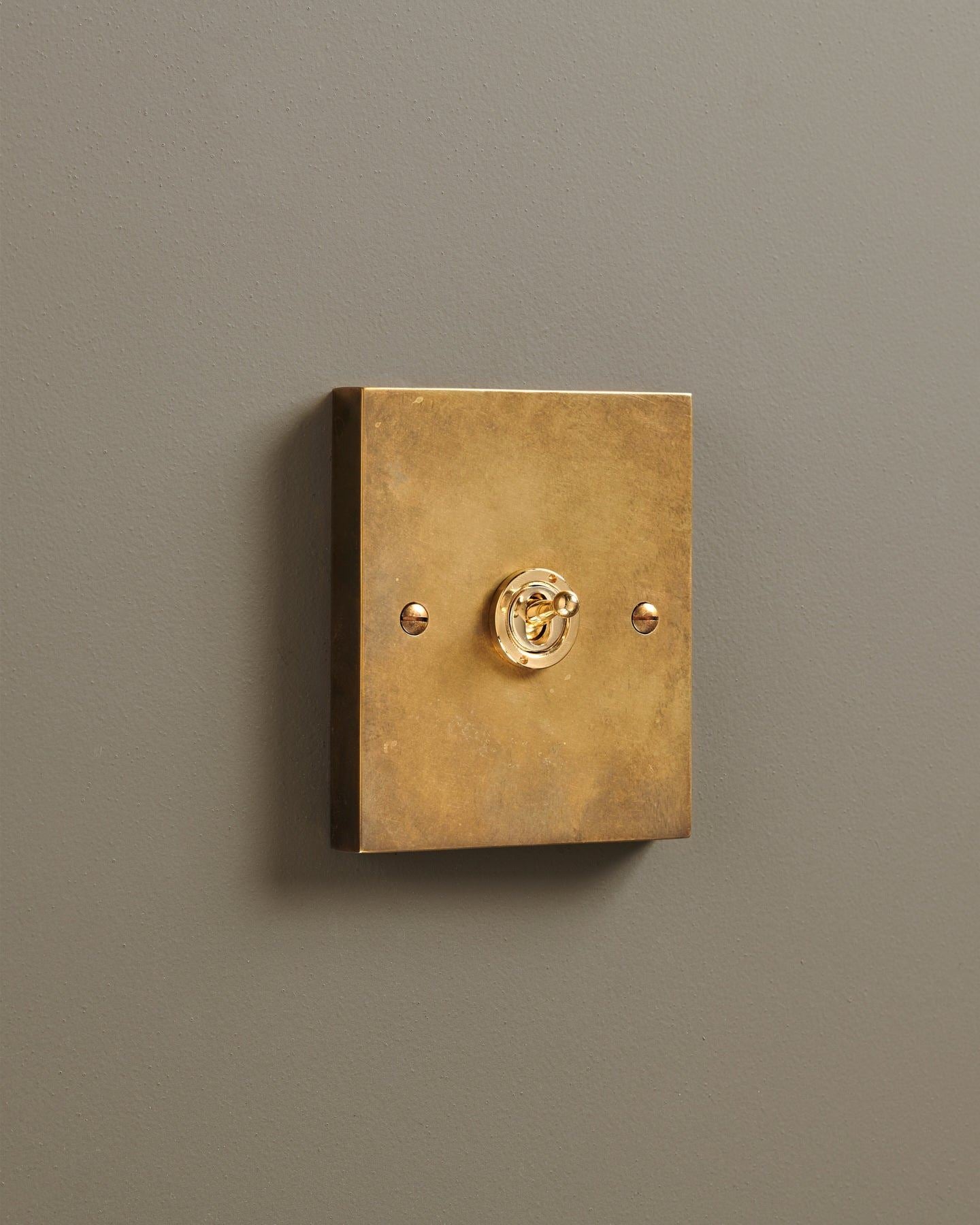 An oblique view of a 1 gang box toggle switch in a warm burnished brass finish.