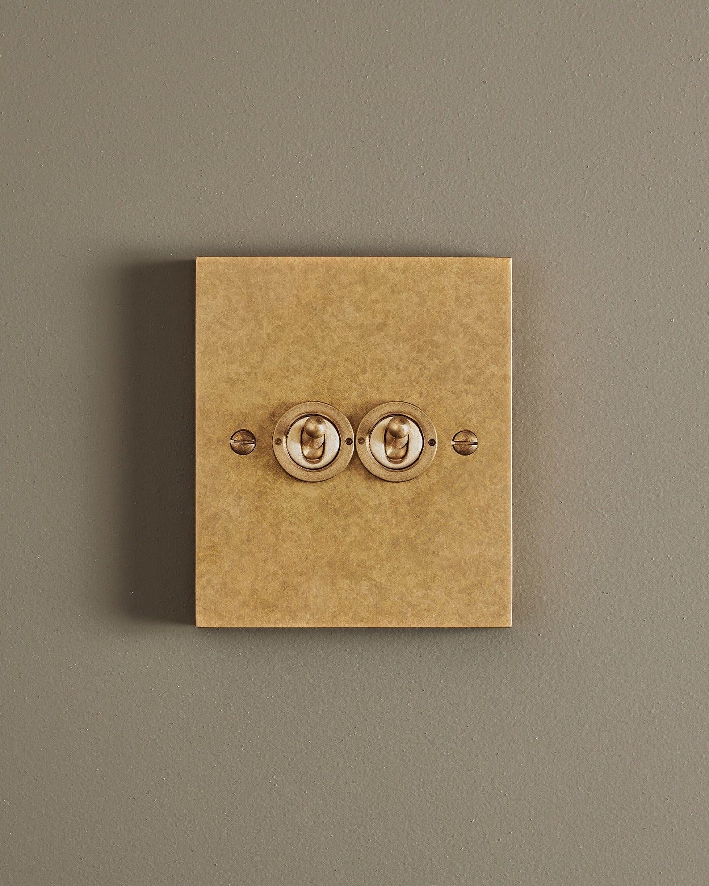 A straight-on view of a 2 gang box toggle switch in a mottled aged brass finish.