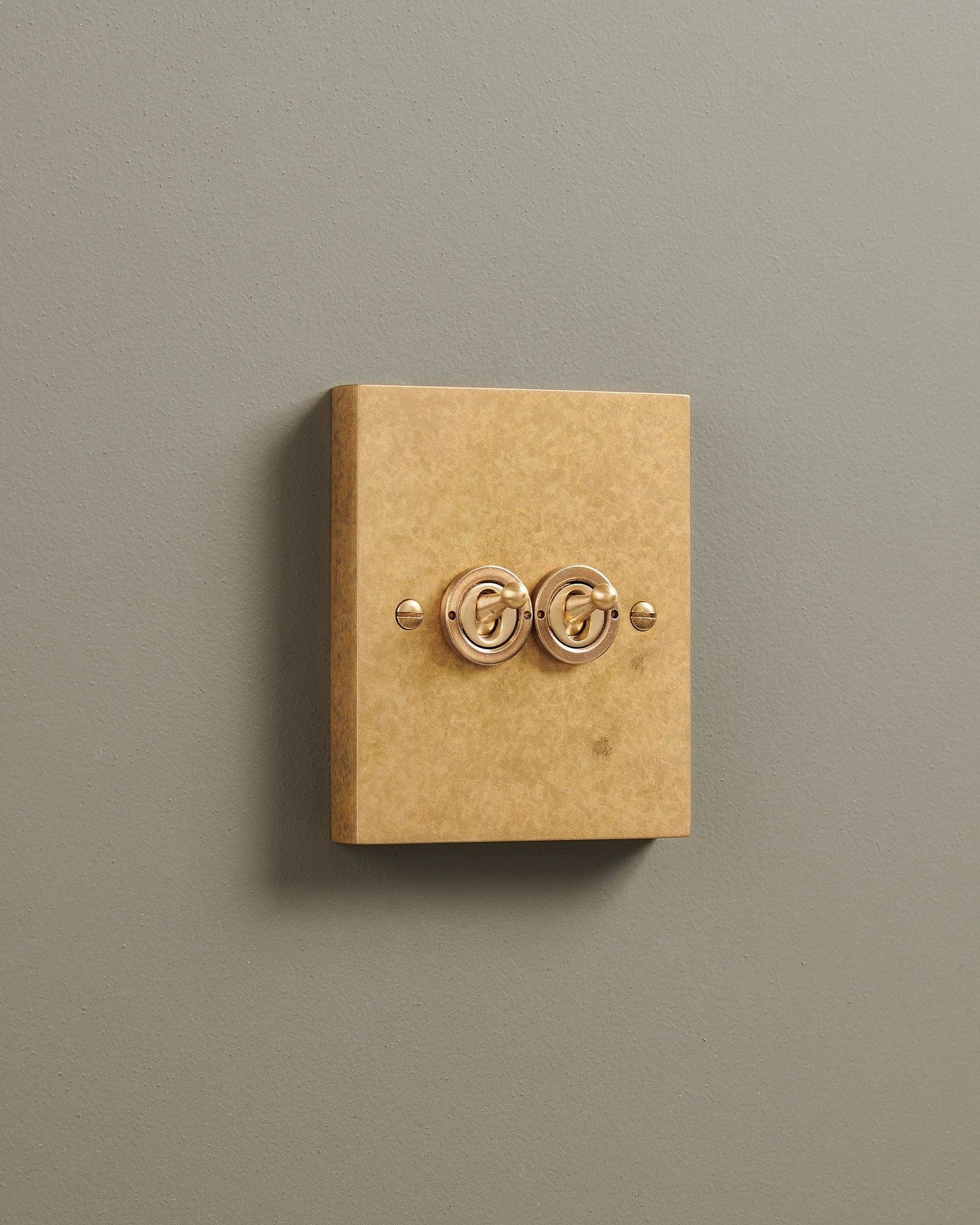 An oblique view of a 2 gang box toggle switch in a mottled aged brass finish.
