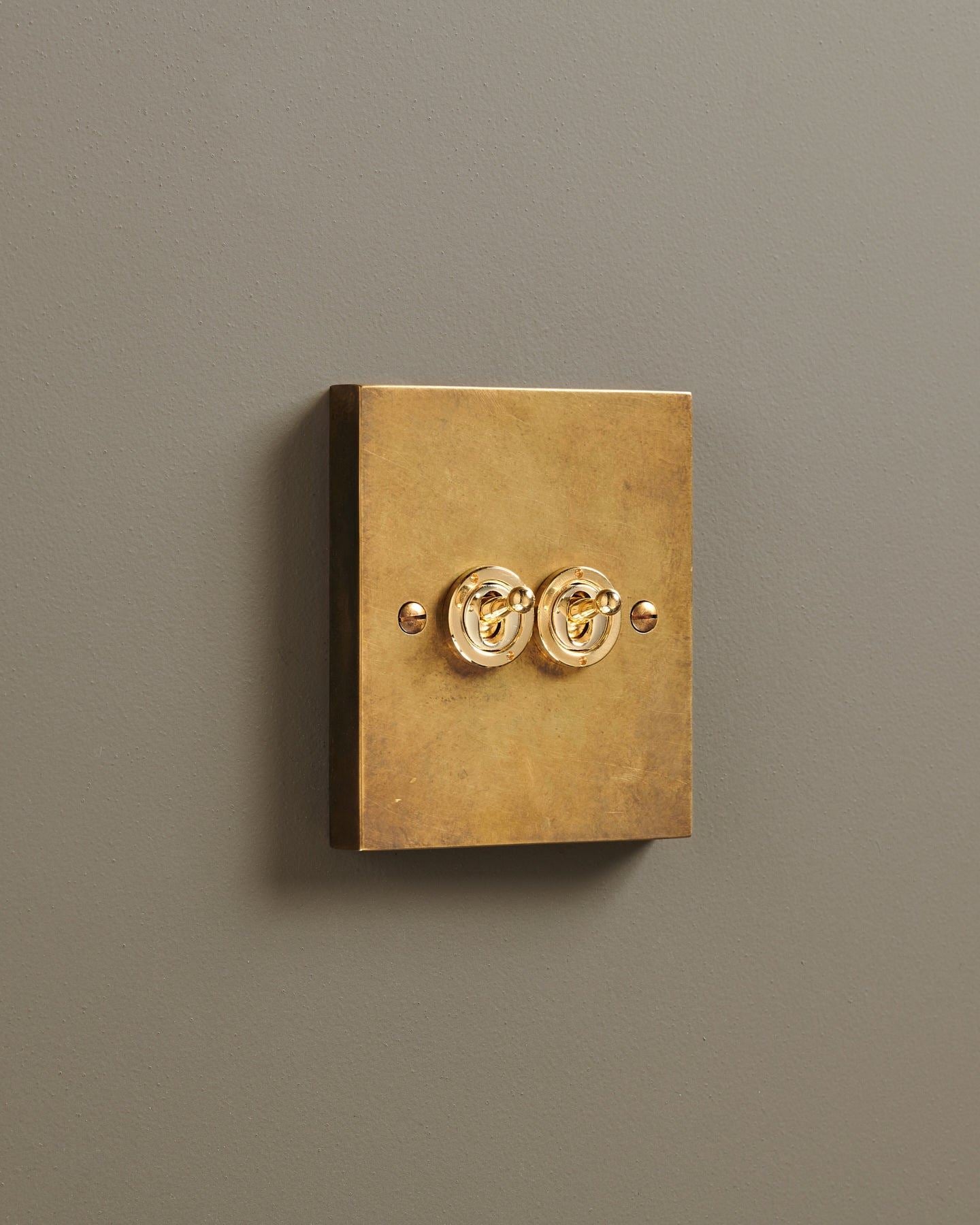 An oblique view of a 2 gang box toggle switch in a warm burnished brass finish.