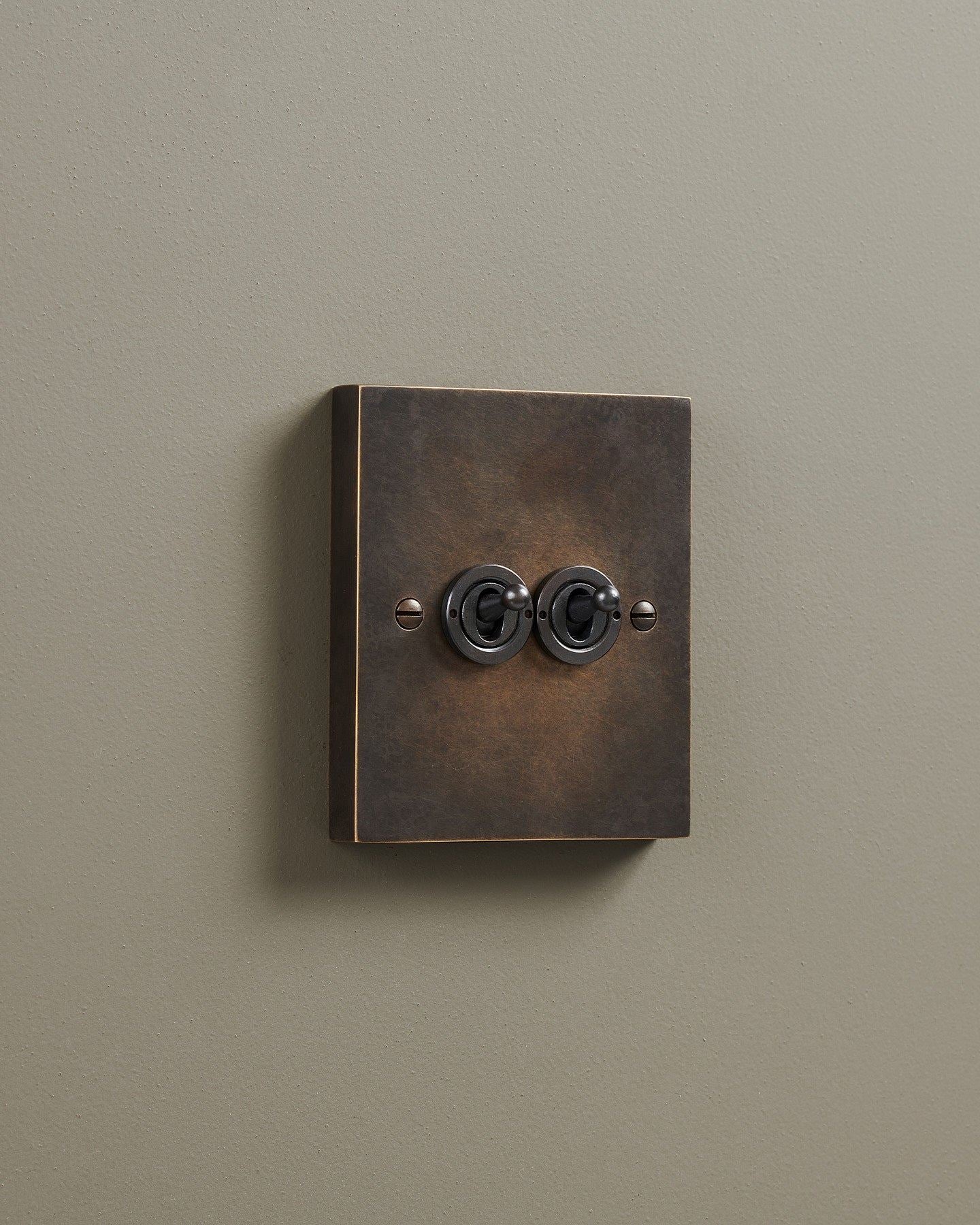 An oblique view of a 2 gang box toggle switch in a dark oxidised brass finish.