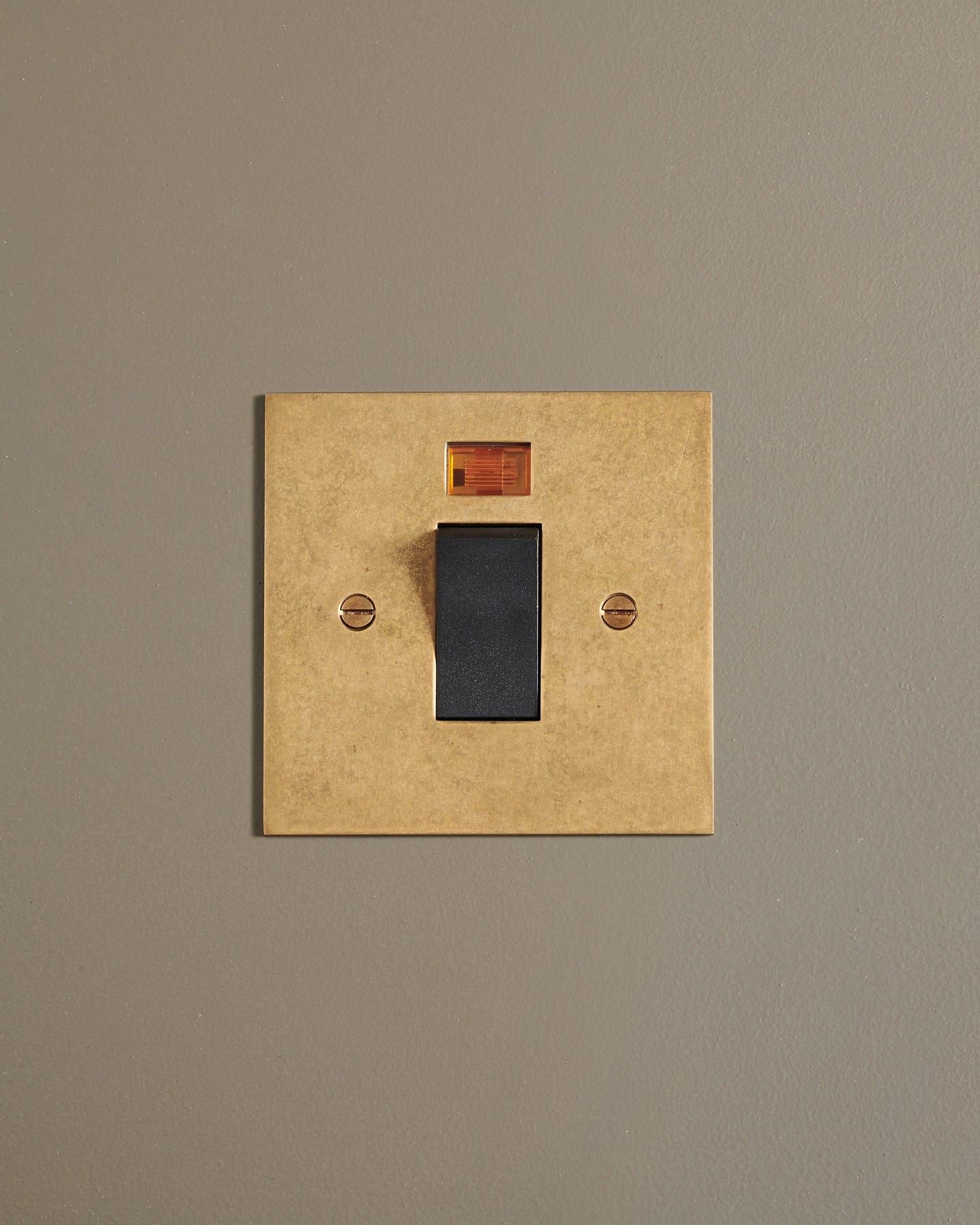 A straight-on view of a classic 45 amp cooker switch in a mottled aged brass finish.