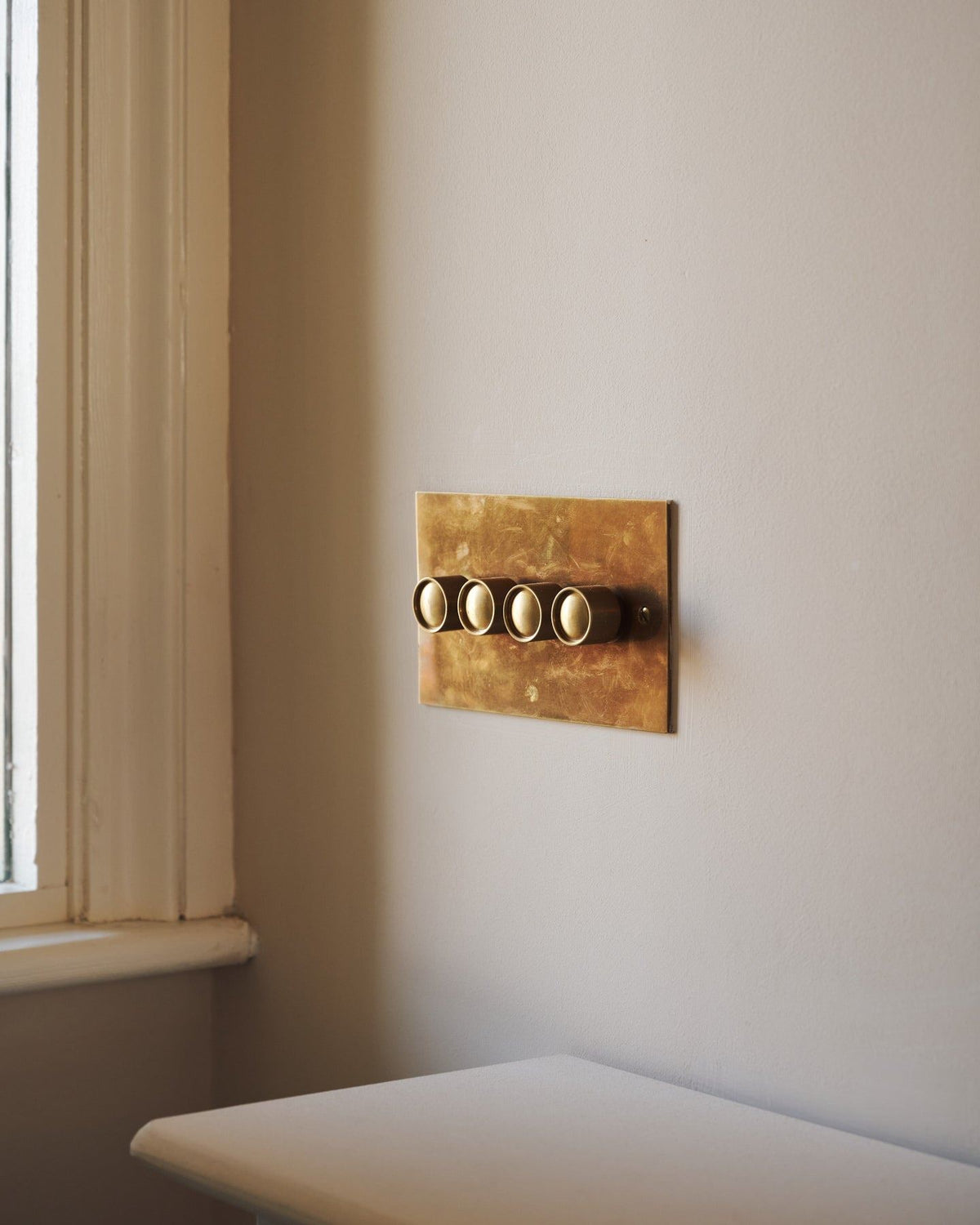 An oblique view of a 4 gang classic dimmer switch in a warm burnished brass finish on soft pink walls with light painted woodwork.|Heirloom Brass shown TEST