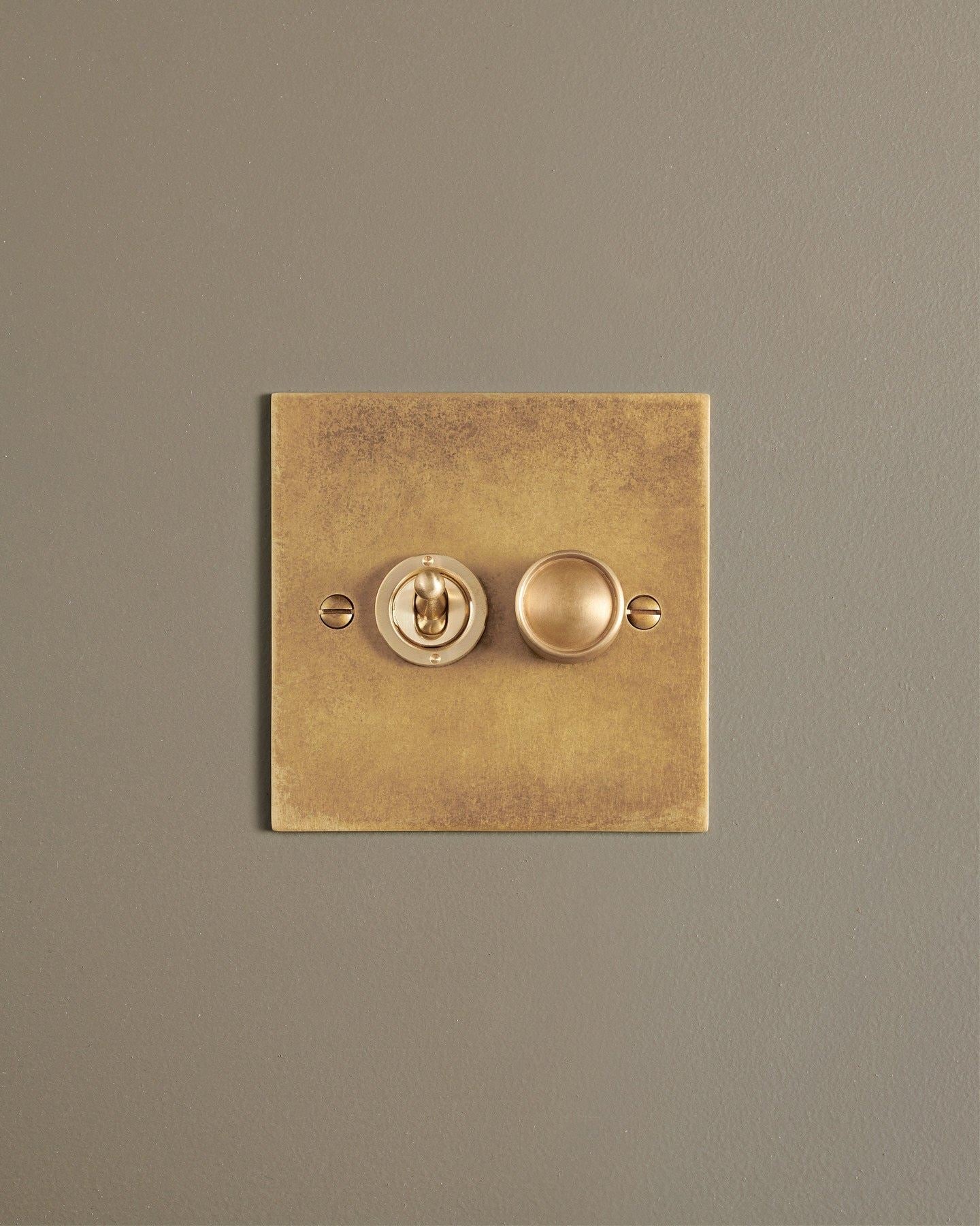 A straight-on view of a 2 gang classic toggle and dimmer mixed switch in a mottled aged brass finish.