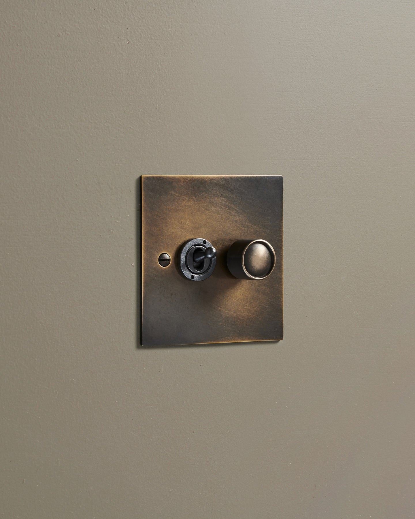 An oblique view of a 2 gang classic toggle and dimmer mixed switch in a dark oxidised brass finish.