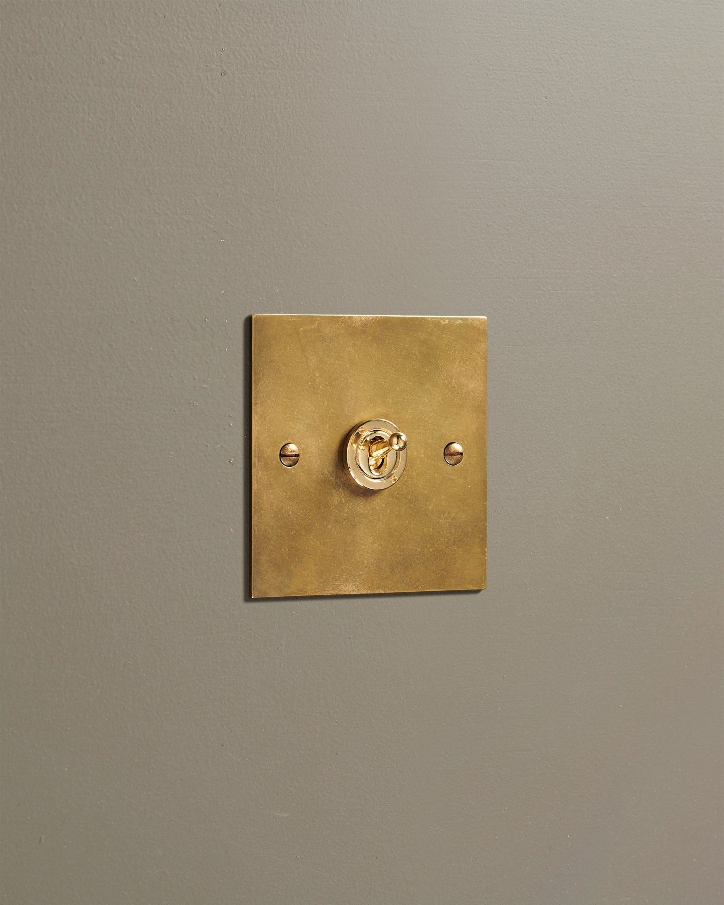 An oblique view of a 1 gang classic toggle switch in a warm burnished brass finish.