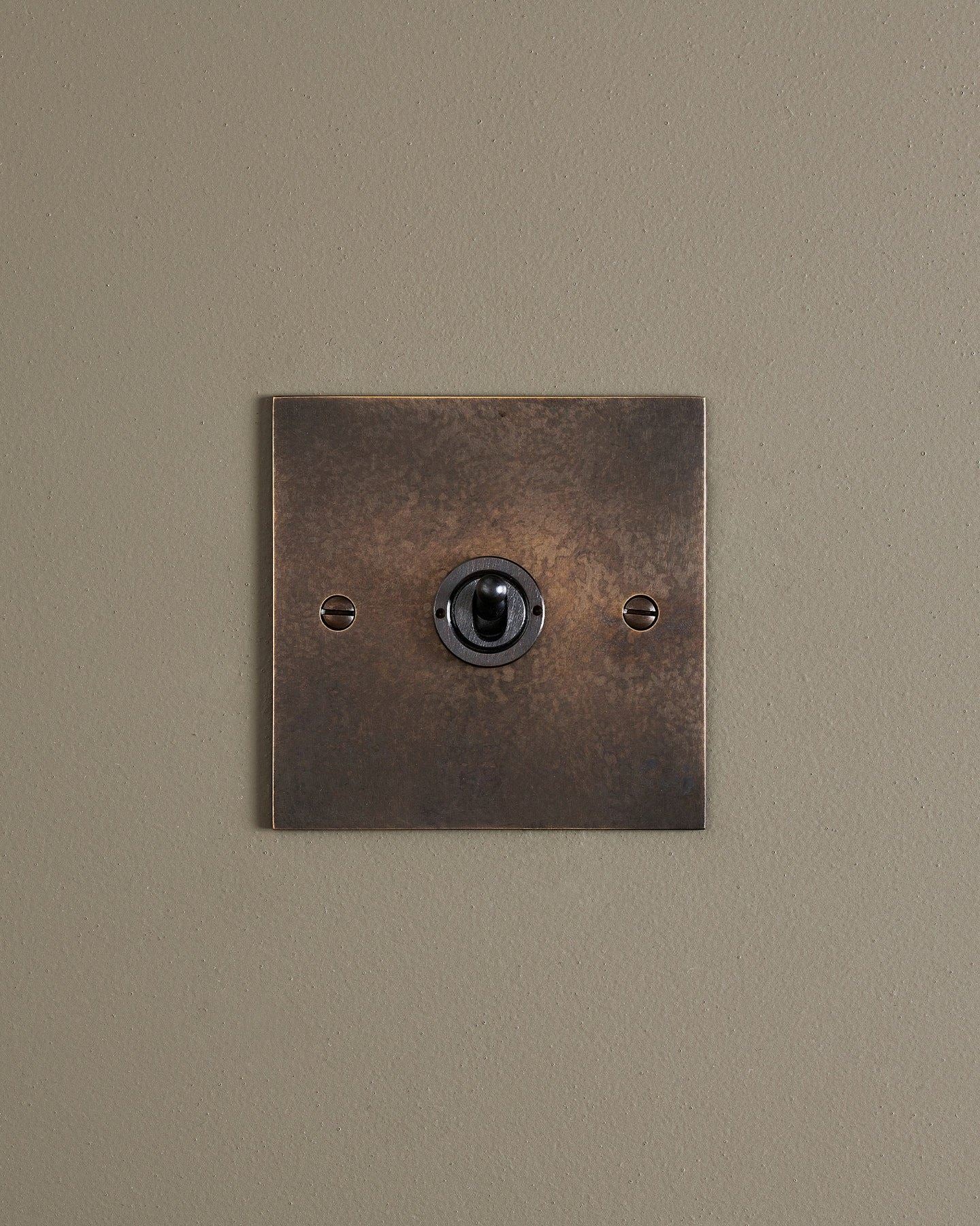 A straight-on view of a 1 gang classic toggle switch in a dark oxidised brass finish.