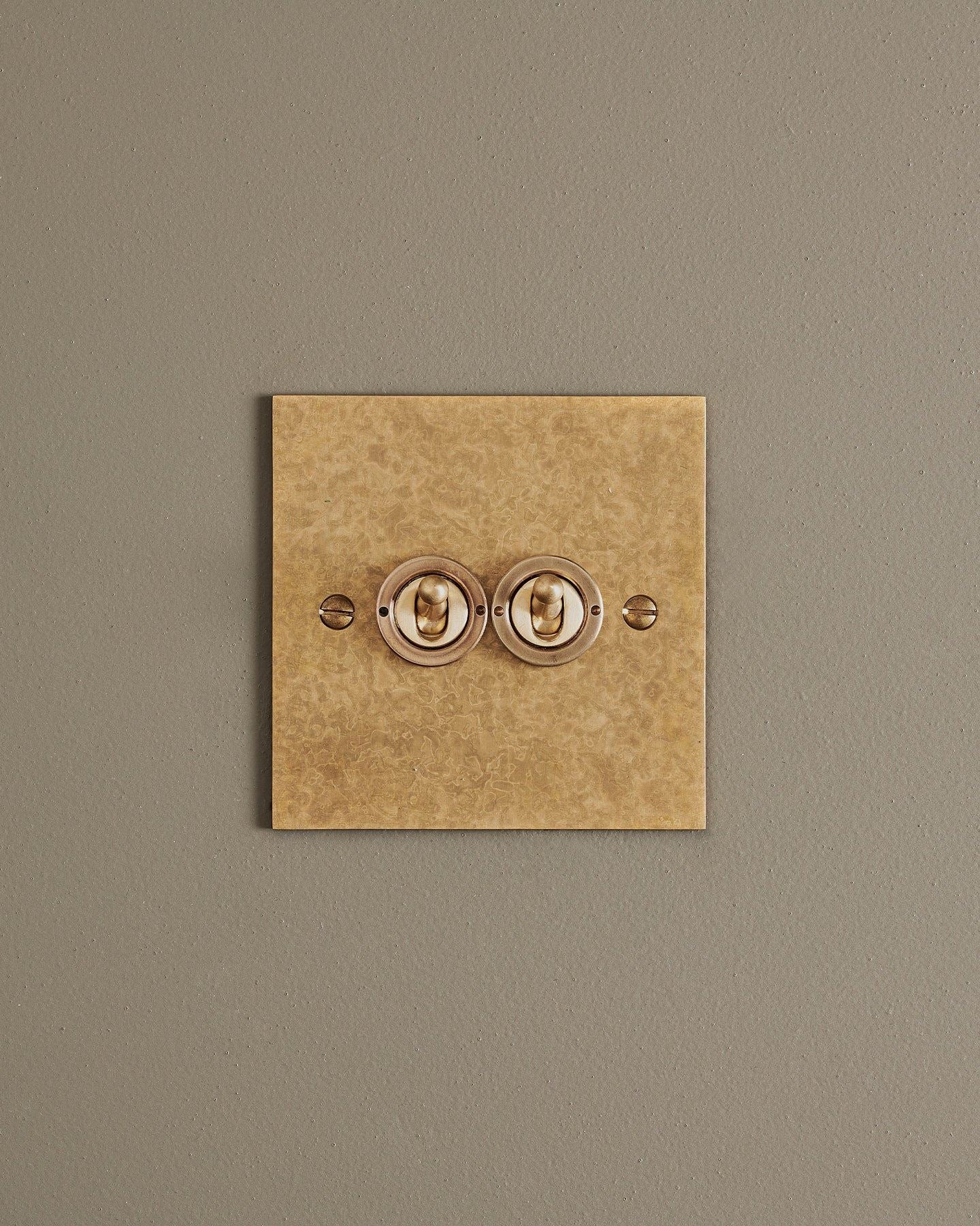 A straight-on view of a 2 gang classic toggle switch in a mottled aged brass finish.