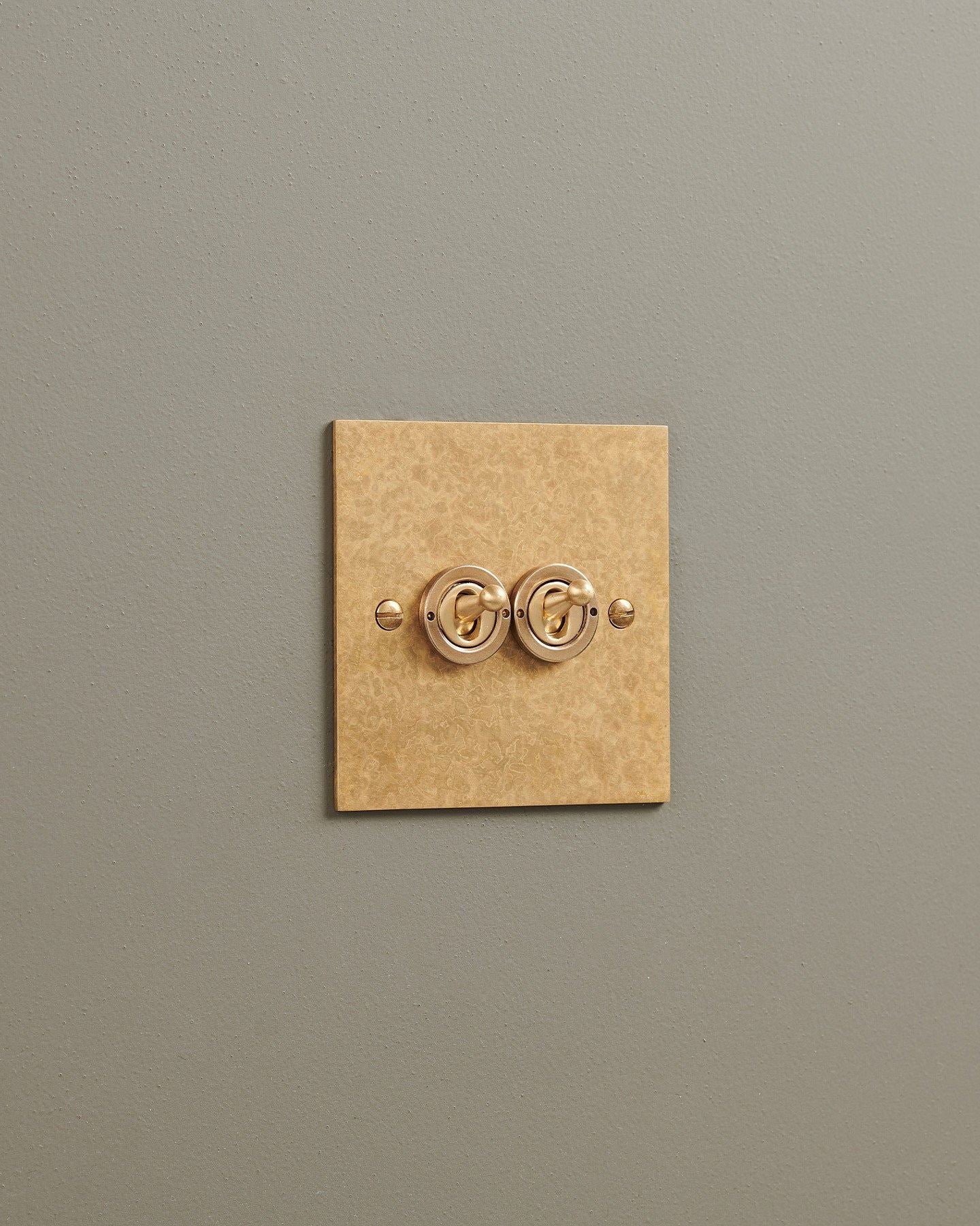 An oblique view of a 2 gang classic toggle switch in a mottled aged brass finish.