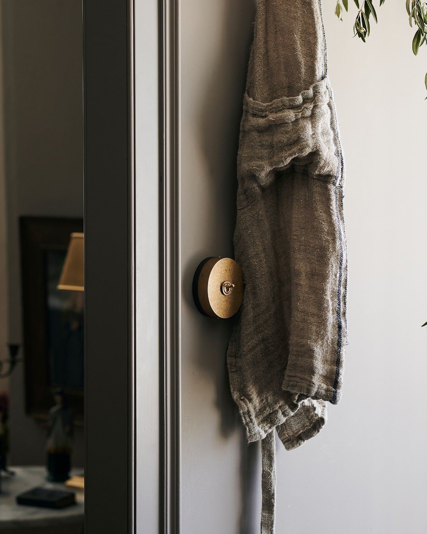 A 1 gang oval-shaped toggle switch in aged brass on a grey wall, hiding behind a vintage linen apron.