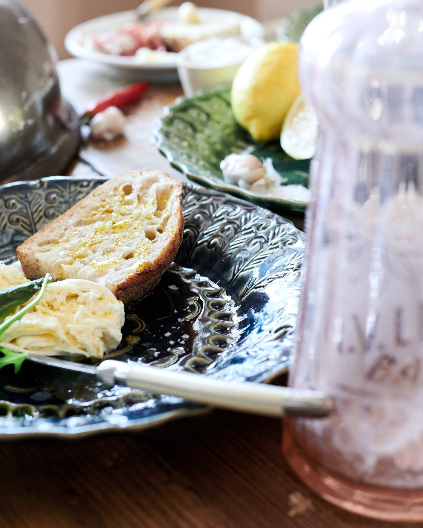 A close-up view of a round handmade bohemian-style blue ceramic platter with vintage silverware, cheese and homemade bread.