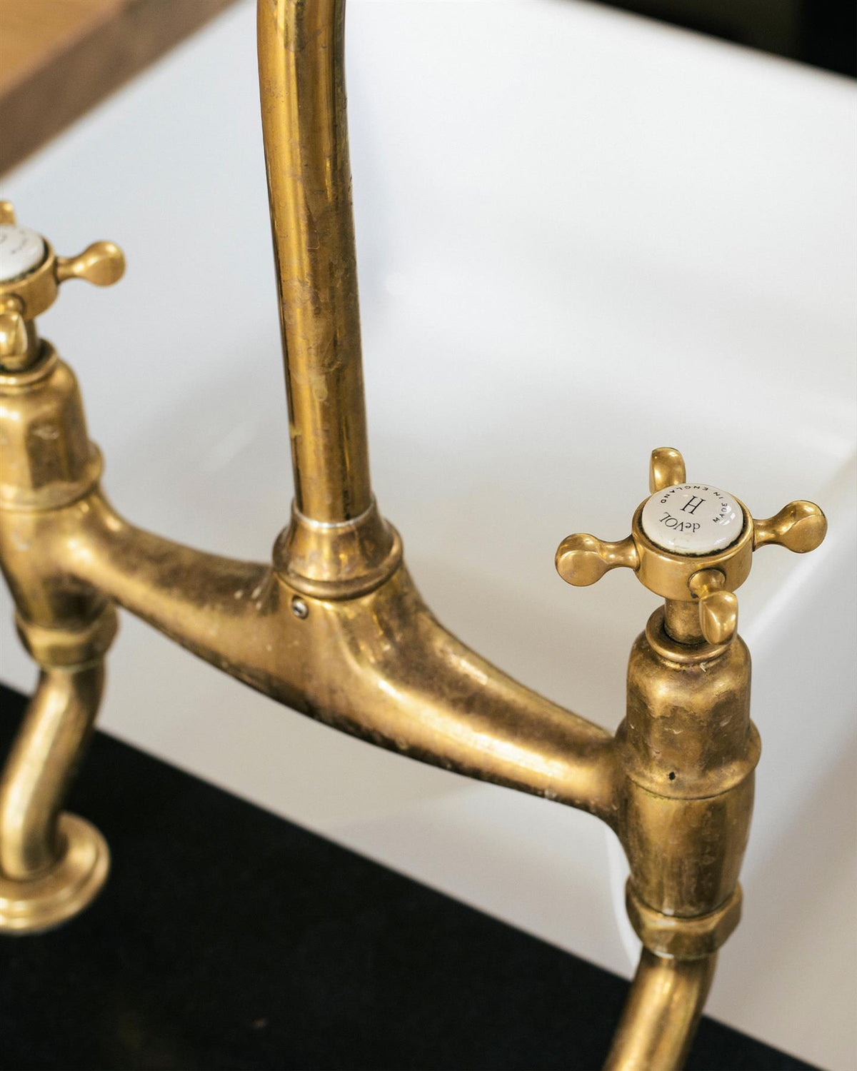 A close-up view of a crosshead handle of a traditional-style aged brass mixer tap. An 'H' can be seen in the centre of the handle with the words 'deVOL' and 'Made in England' around the perimeter. TEST