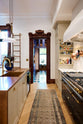 Past a grand and spacious classic English kitchen features a half vintage and half deVOL kitchen island with a copper sink and a cooker run with an Arabescato marble worktop is a blue walk-in pantry. Beautifully decorated with artisan glass and ceramics, a sophisticated floral arrangement, an aged brass hanging rail, a bespoke ladder, and milk glass pendant lights, it creates a social space with a touch of luxury.
