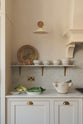 A close and oblique view of a grand yet understated Classic English kitchen, this space features a sink run with reeded glazed wall cupboards, full-height cabinetry, and an island with a Carrara marble worktop. Styled with vintage artisan ceramics and a bowl of fresh green pears, it feels wonderfully light, airy, and perfectly suited to relaxed, sociable living.
