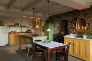 The quaint and glamorous cottage kitchen, in shades of green and scullery yellow, includes a small sink run with an oak countertop, an aged brass Ionian tap, glazed wall cabinets, freestanding cupboards, and a marble-topped base cabinet. Lovingly decorated with vintage furniture, ceramics, and deVOL Heirloom gaselier lights, the space exudes personality and charm while respecting the cottage's original textures.