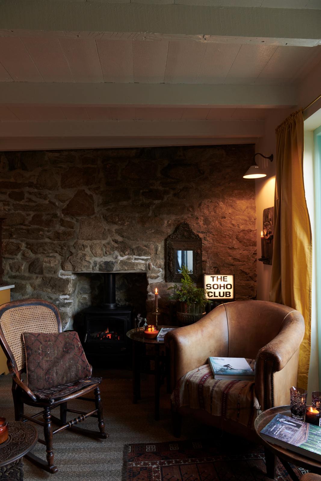 A quiet corner of the quaint and glamorous cottage is lovingly decorated with vintage furniture, books, an iron fireplace, “The Soho Club” light box, and a deVOL mini creamware wall light. The space exudes personality and charm while respecting the cottage's original textures.