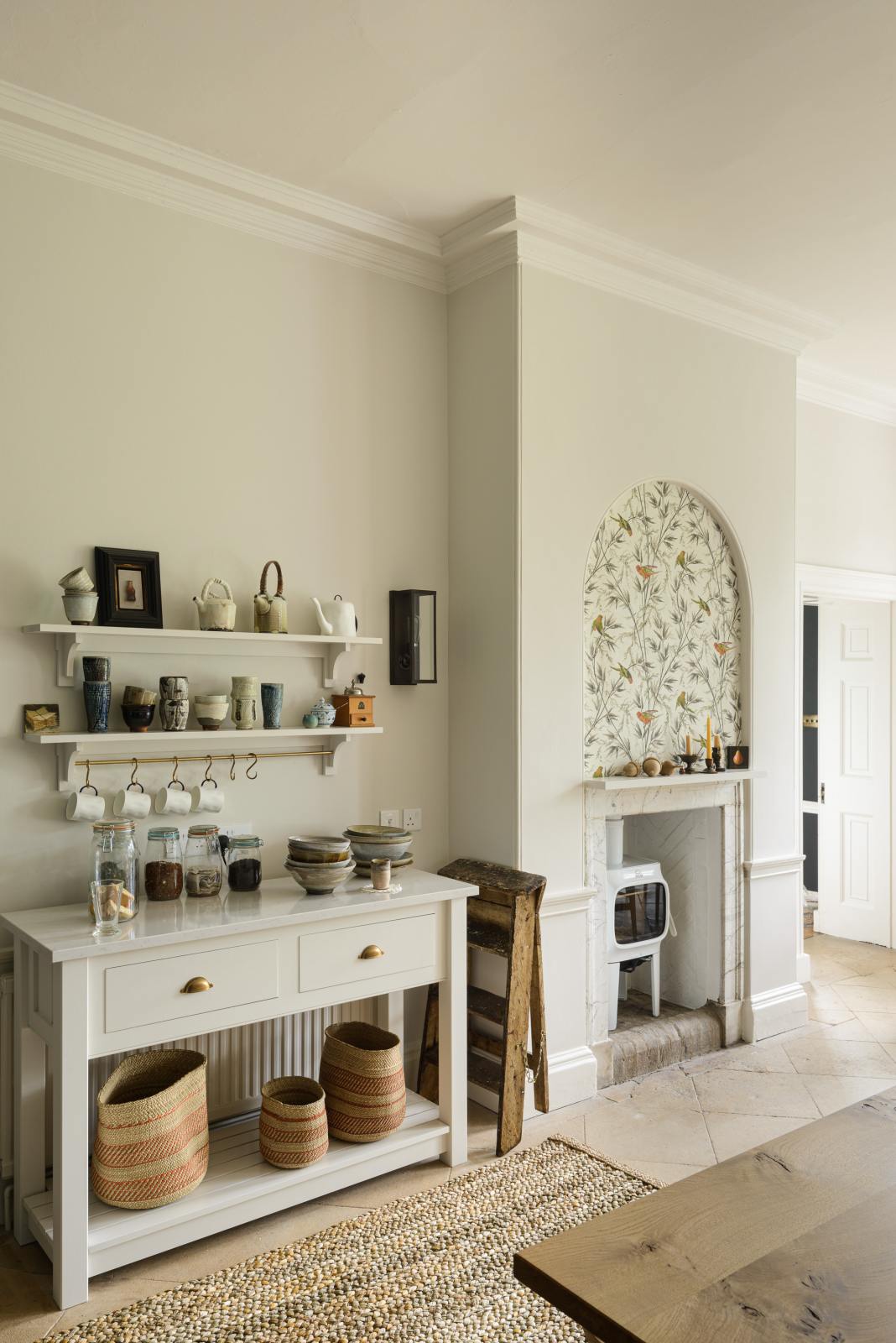 A small section of the renovated medieval house’s kitchen is a drinking station with a white linen prep table, a Silestone worktop, and shelves with a brass hanging rail. It is elegantly adorned with vintage furniture, artisan ceramics, mugs, and a collection of teas and coffee beans, seamlessly blending the historical with the contemporary.