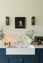 A closer look at a classic English, Bond Street blue kitchen features a cooker and sink run with a Silestone worktop, a double sink, an aged brass Ionian tap, and white crackle metro splashback tiles. The renovated medieval house is elegantly adorned with modern still-life paintings, artisan ceramics, and vibrant green plants, seamlessly blending the historical with the contemporary.