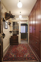 A practical Refectory red corridor with a classic carcass with a double door, full-height cupboards, and peg rail. Pridefully displaying a taxidermy boar, a large rug, and collectable antiques, it embraces a unique museum-like social space.